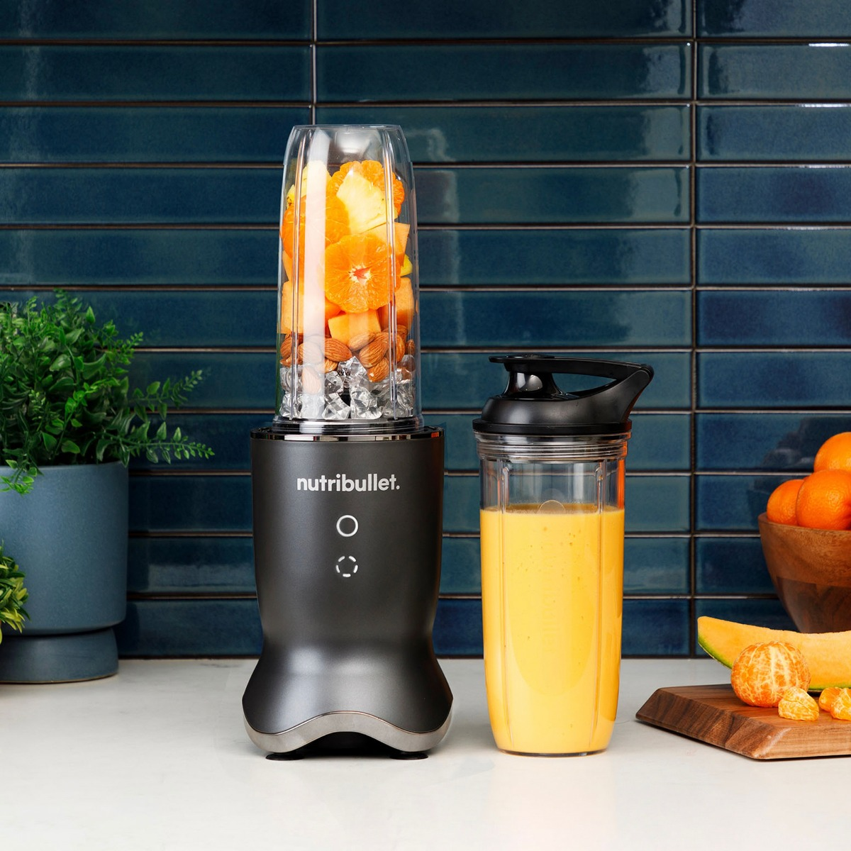 Een zwarte Nutribullet-blender met een volle bak fruit staat naast een smoothie. Op de achtergrond een betegelde muur.