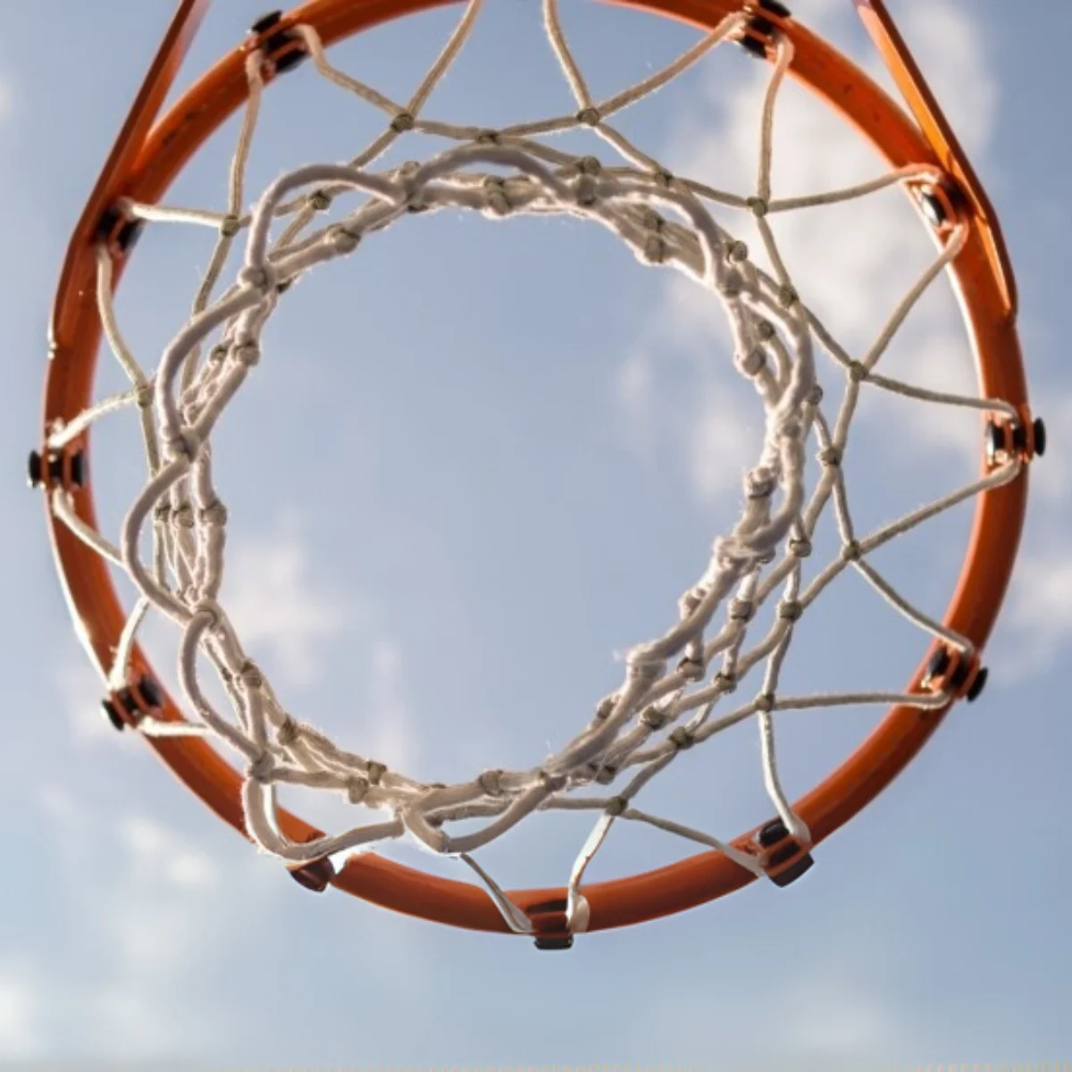 Looking up at a basketball hoop, showing the orange rim and white net against a blue sky.