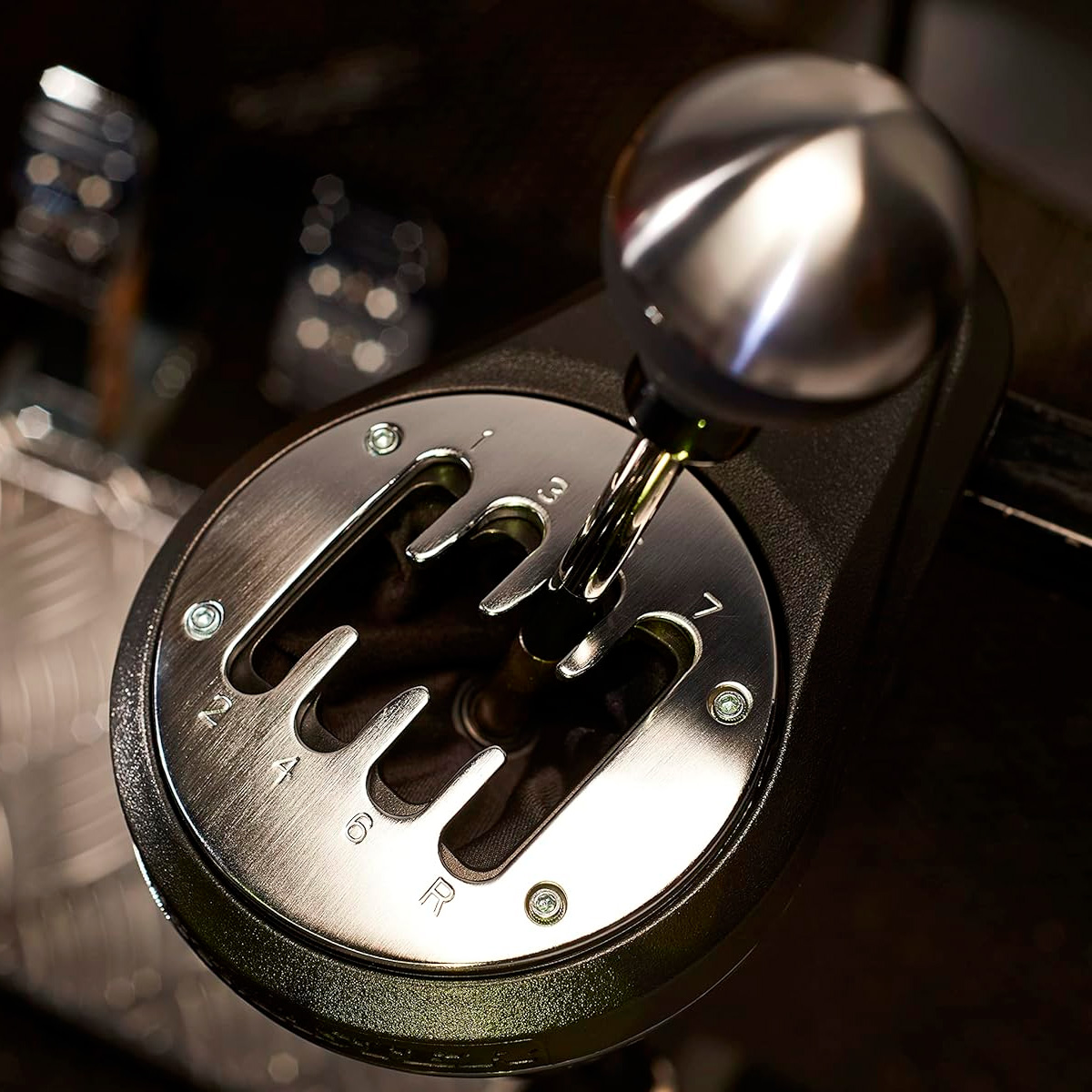 Levier de vitesses avec base métallique et différentes options de vitesse. Le levier de vitesses est argenté et noir, avec des chiffres blancs.