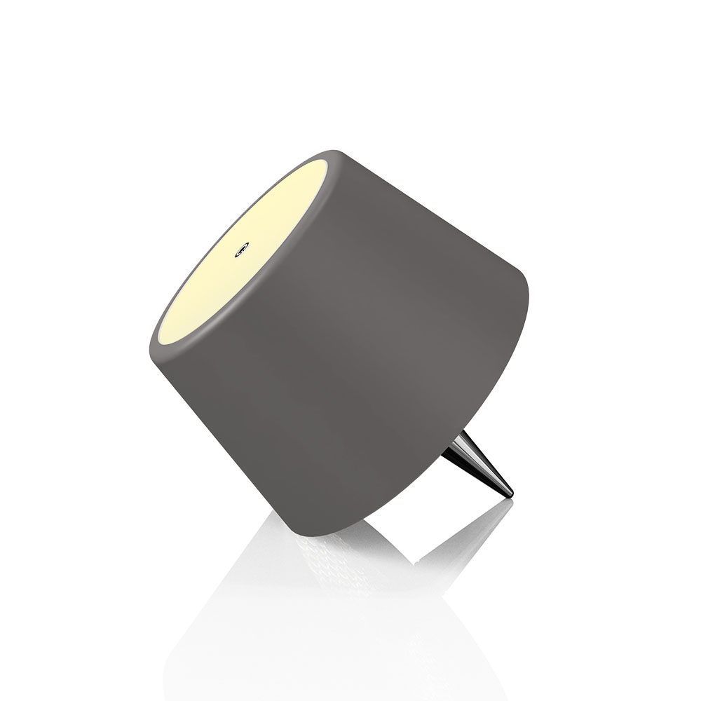 Una lampada grigia con un paralume a forma di cono e una base appuntita rivolta verso il basso, che si riflette su una superficie bianca.