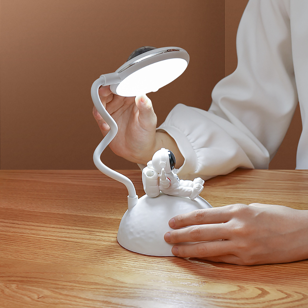 Eine weiße Schreibtischlampe in Planetenform mit einer Astronautenfigur, auf einer Holzoberfläche.