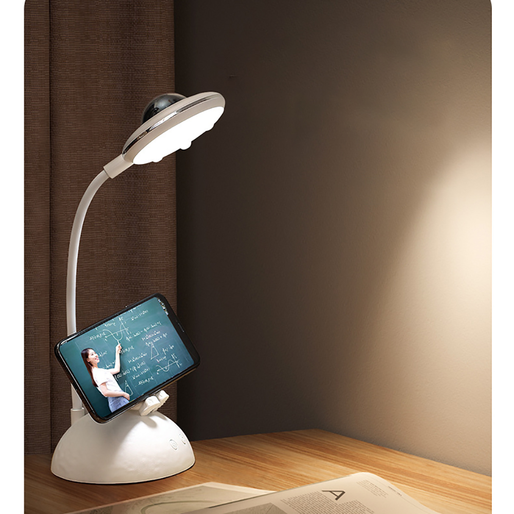 Eine weiße Schreibtischlampe mit Telefonhalterung und Person auf dem Bildschirm. Auf Holzoberfläche.
