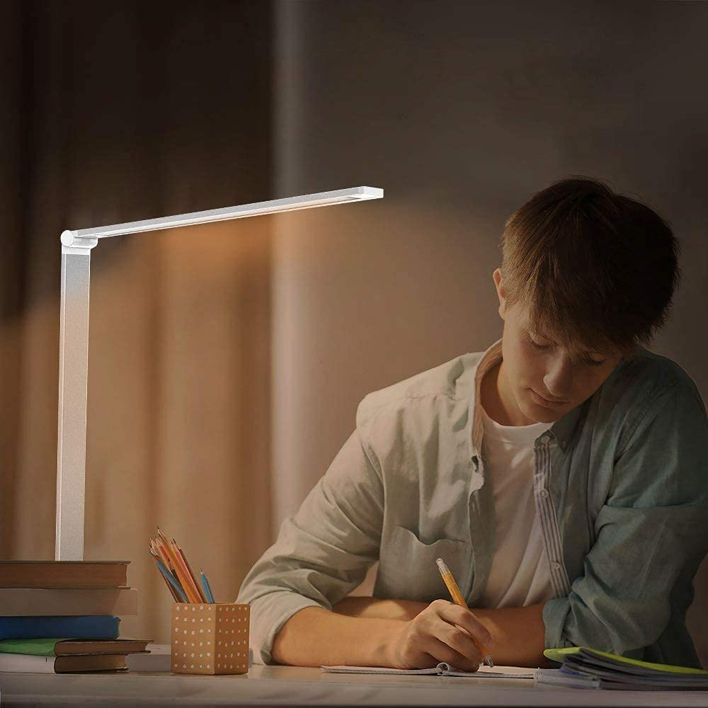 Eine Person schreibt an einem Schreibtisch mit einer Schreibtischlampe, Büchern und Bleistiften.