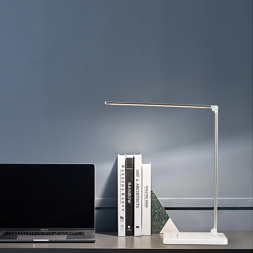 Eine Schreibtischlampe steht auf einem Schreibtisch mit Büchern und einem Laptop. Der Hintergrund ist eine blaue Wand.