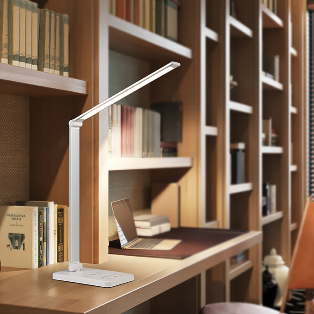 Eine weiße Schreibtischlampe steht auf einem Schreibtisch. Bücherregale sind im Hintergrund.