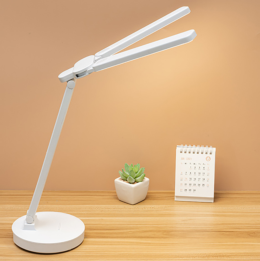 Eine weiße Schreibtischlampe mit verstellbaren Lichtpaneelen auf einem Schreibtisch, neben Sukkulente und Kalender.