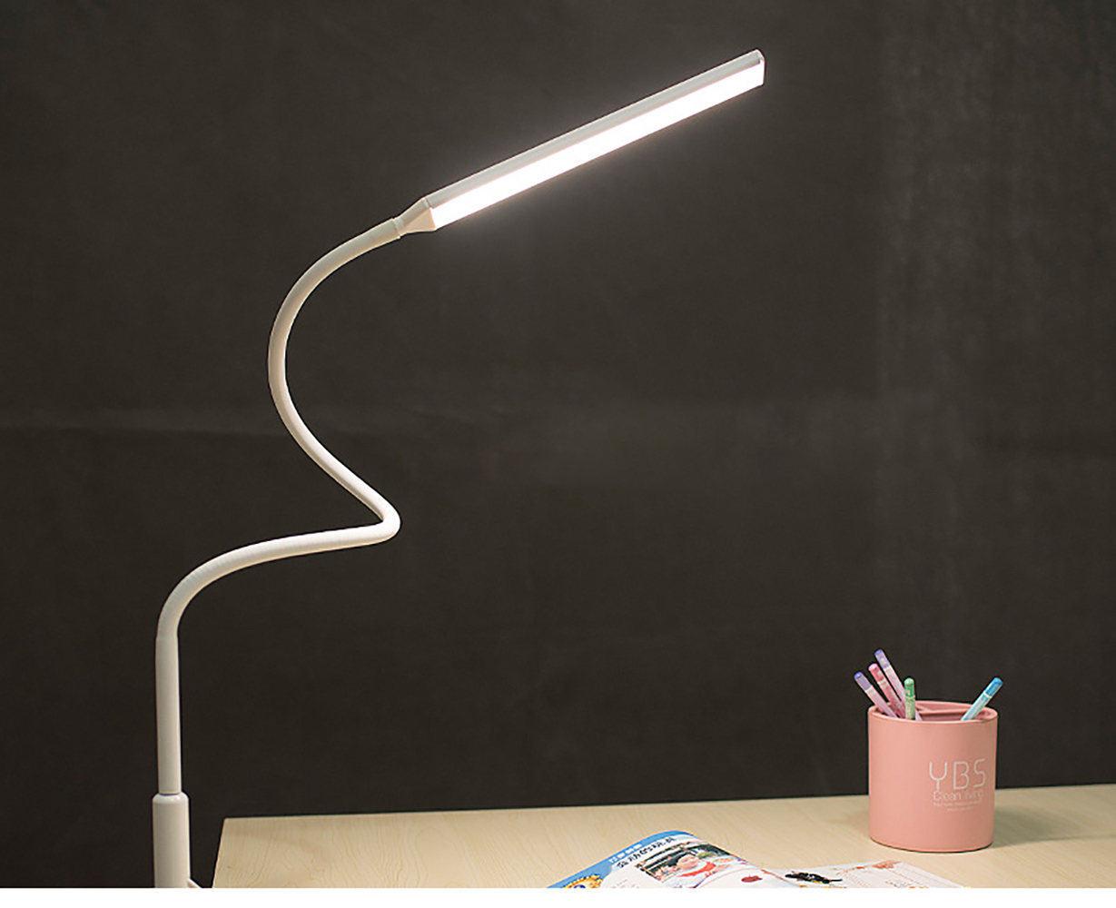 Eine weiße Schreibtischlampe mit gebogenem Arm, auf dunklem Hintergrund, mit rosa Stifthalter.