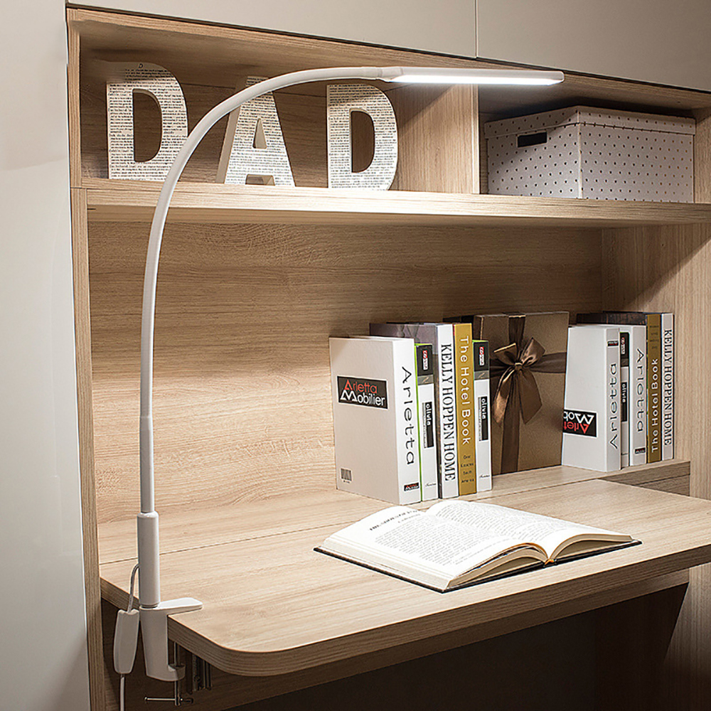 Eine weiße Schreibtischlampe auf einem Schreibtisch. Bücher und ein Schild mit dem Wort DAD sind sichtbar.