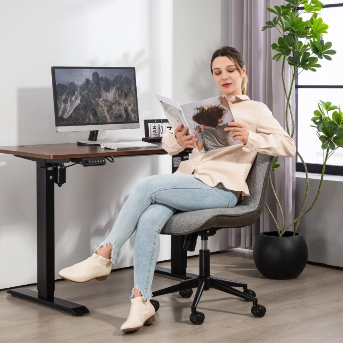 Eine Frau sitzt an einem Schreibtisch mit einem Computer und liest eine Zeitschrift.