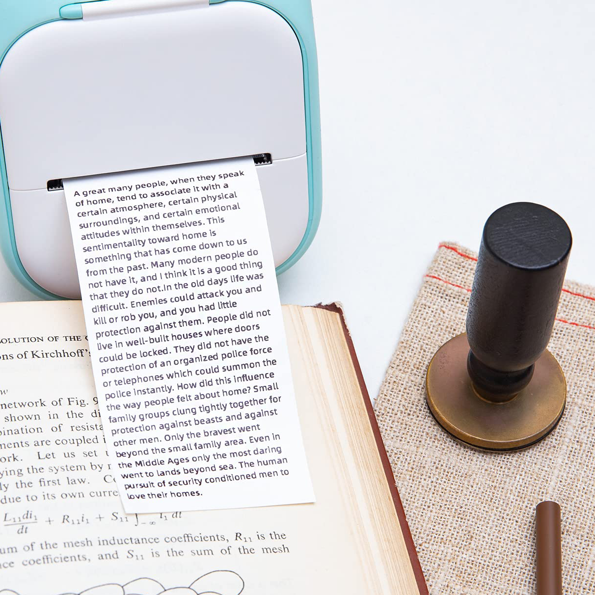Ein kleiner Drucker mit Textausgabe auf Papier. Buch und Stempel sind im Hintergrund.