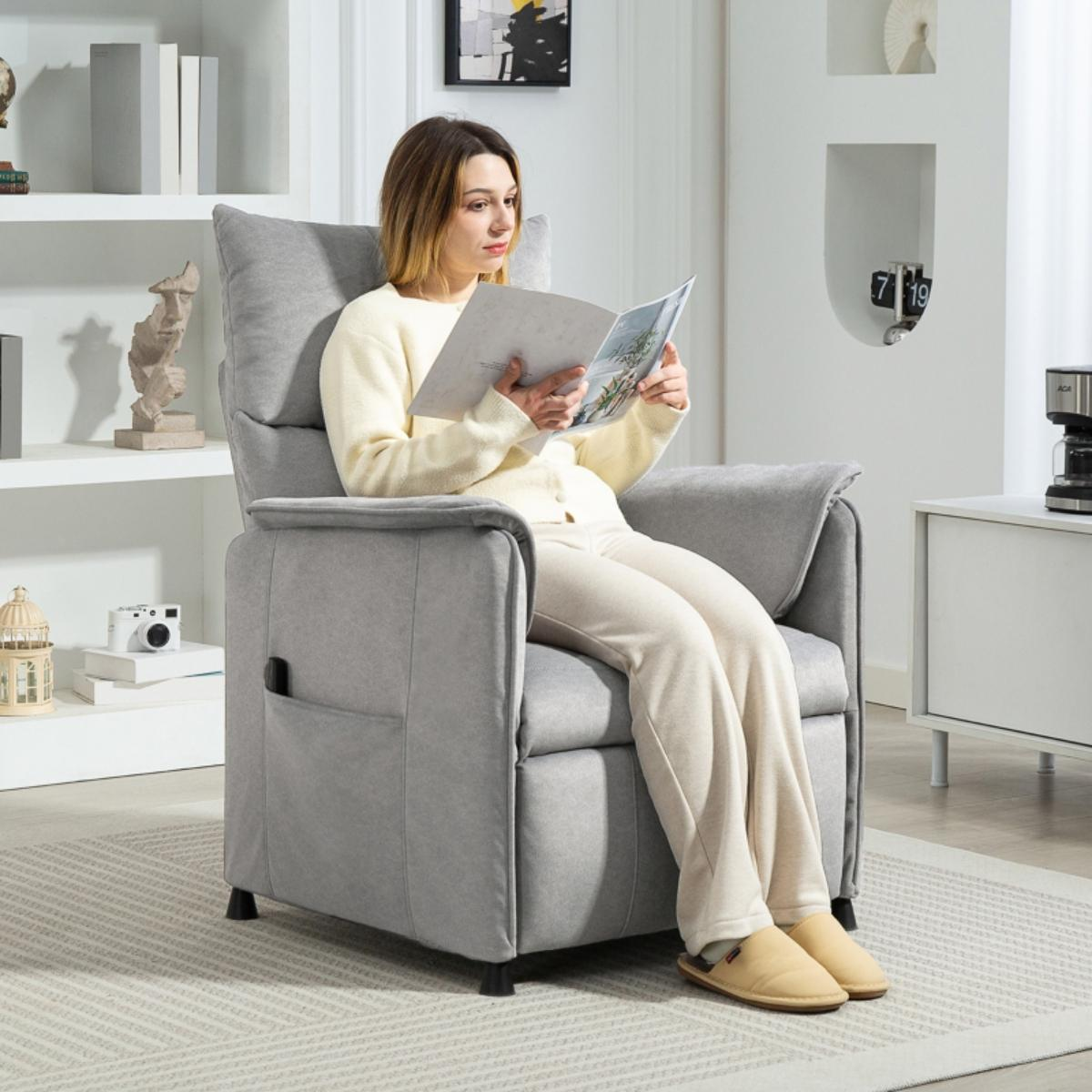Eine Frau sitzt in einem grauen Relaxsessel und liest ein Buch. Der Raum hat eine neutrale Farbpalette und einen Couchtisch.