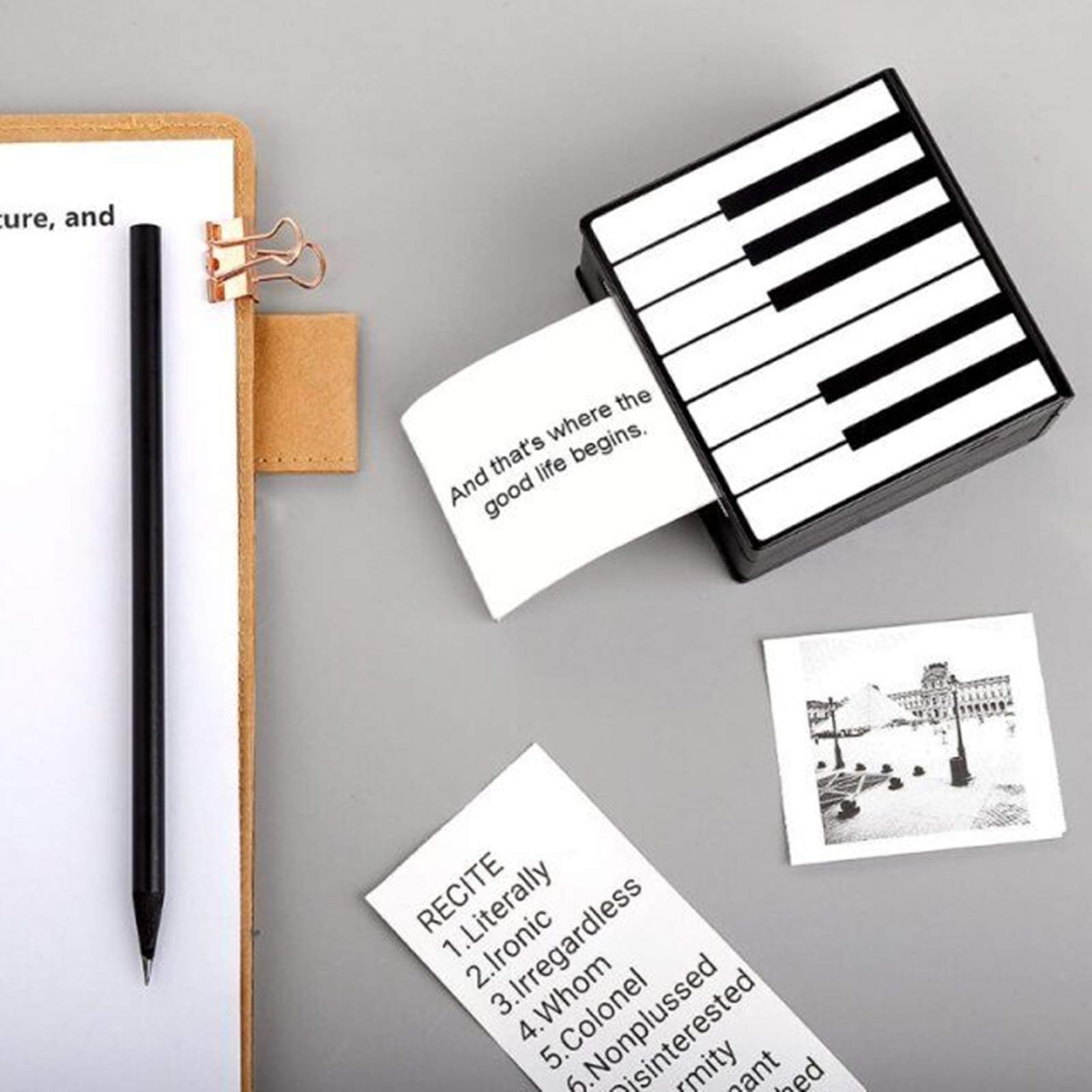 Ein klavierförmiger Drucker steht auf einer Oberfläche mit gedruckten Notizen, einem Stift und einer Klammer. Eine Wortliste ist ebenfalls vorhanden.