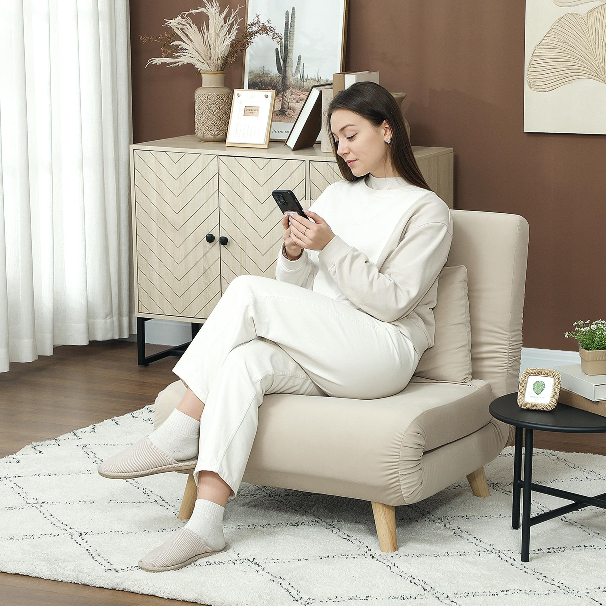 Eine Frau in weißer Kleidung sitzt auf einem beigefarbenen Stuhl und benutzt ihr Handy. Der Hintergrund hat einen Teppich, einen Schrank und Dekorationsartikel.