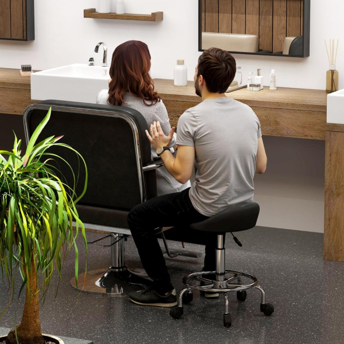 Ein Mann und eine Frau sitzen in einem Friseursalon. Die Frau sitzt auf einem Stuhl, der Mann auf einem Hocker.