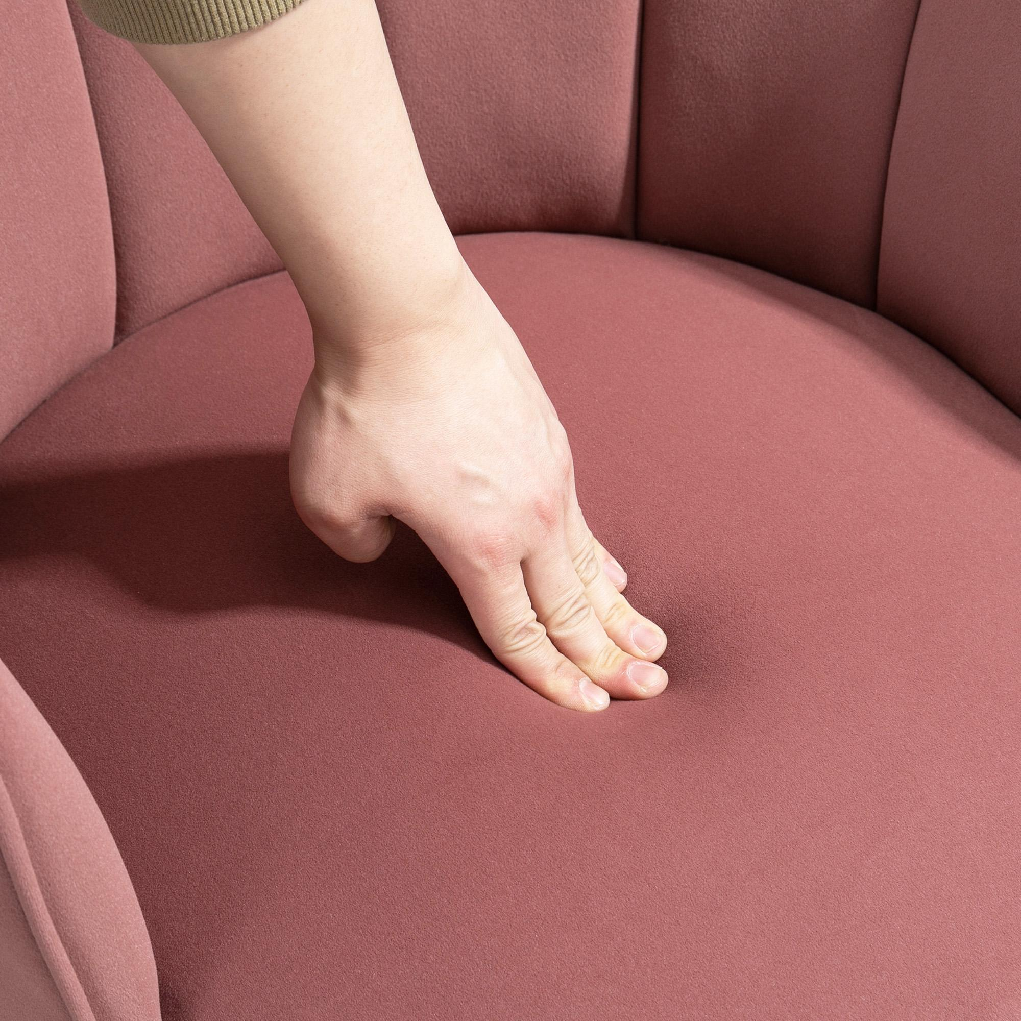 Eine Hand drückt auf den Stoff eines rosa Stuhls und zeigt die Textur und Weichheit des Materials.