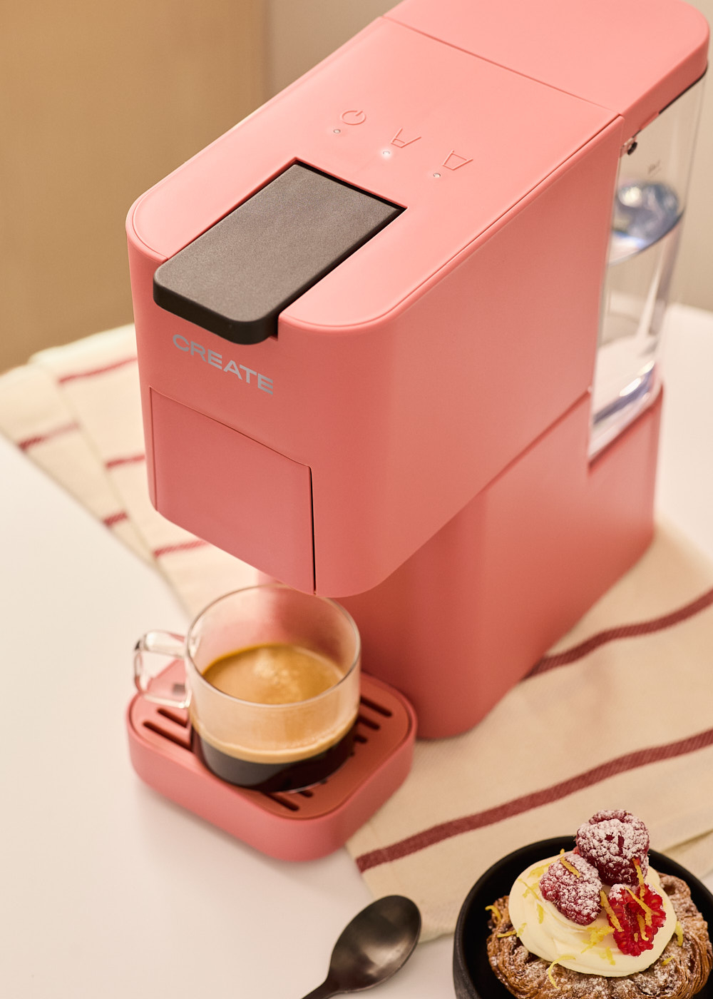 Una cafetera CREATE rosa se ve de cerca sobre una superficie blanca.