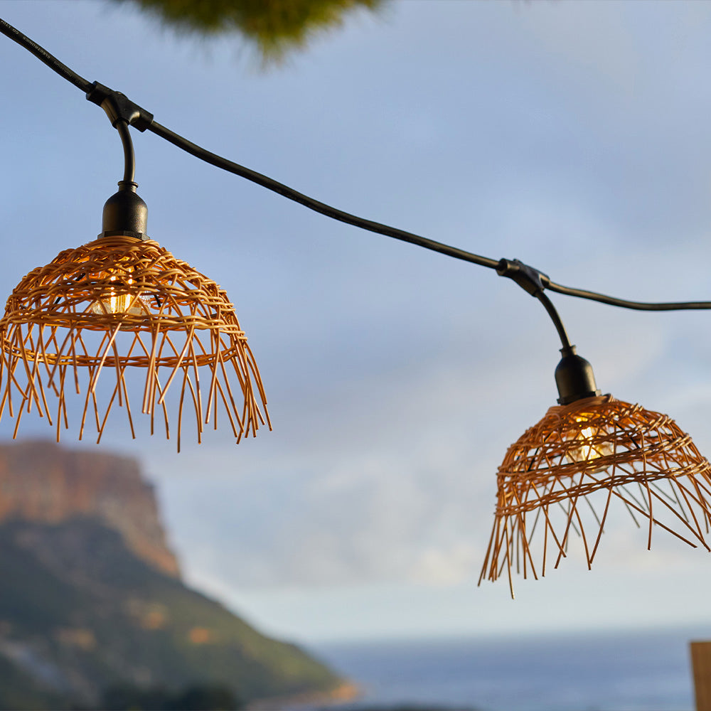 Zwei gewebte Lampen hängen an einem Draht vor einem verschwommenen Hintergrund aus Meer und Himmel.