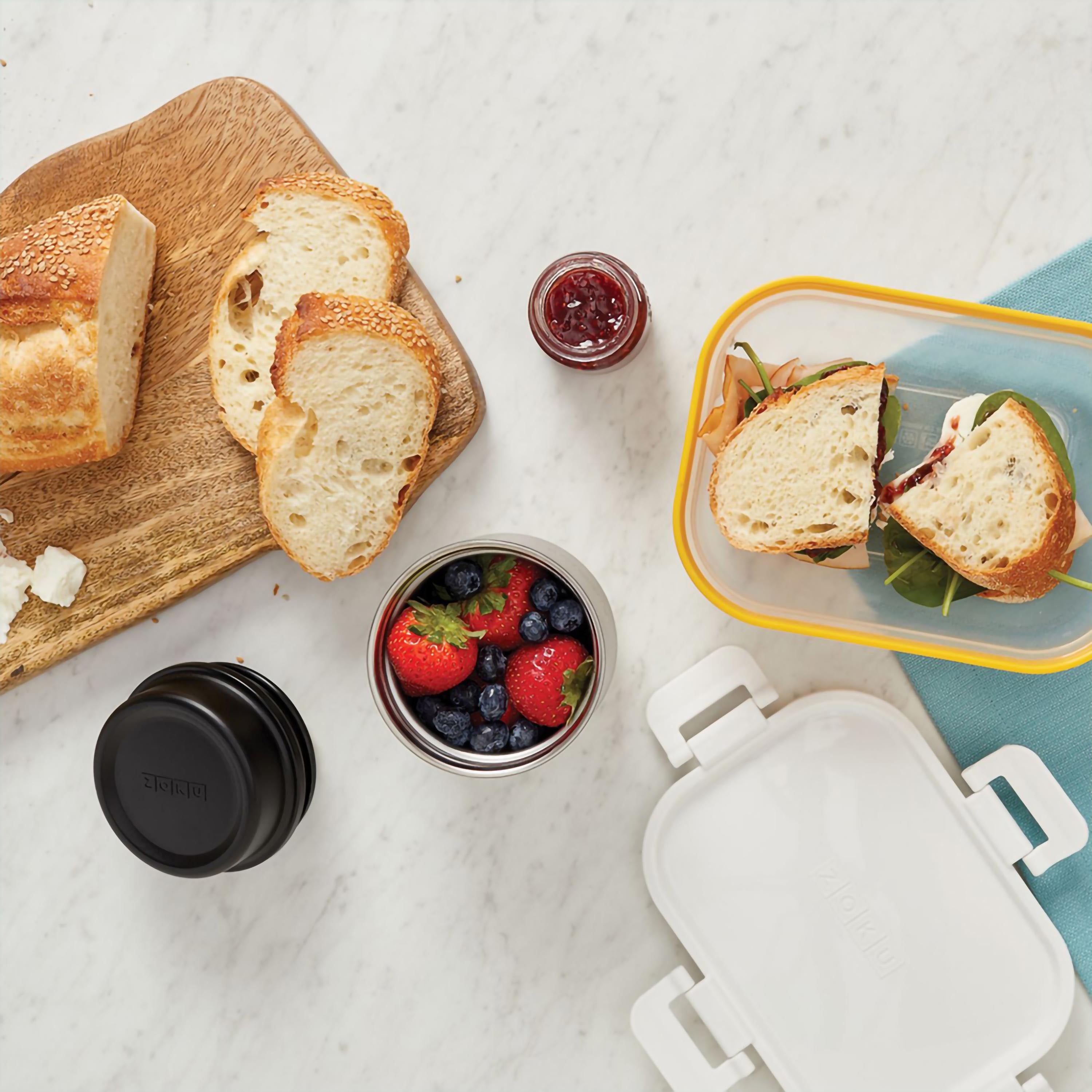 Draufsicht auf Lebensmittel: Brot, Beeren, Sandwich, Marmelade und ein Behälter, mit weißem Hintergrund.