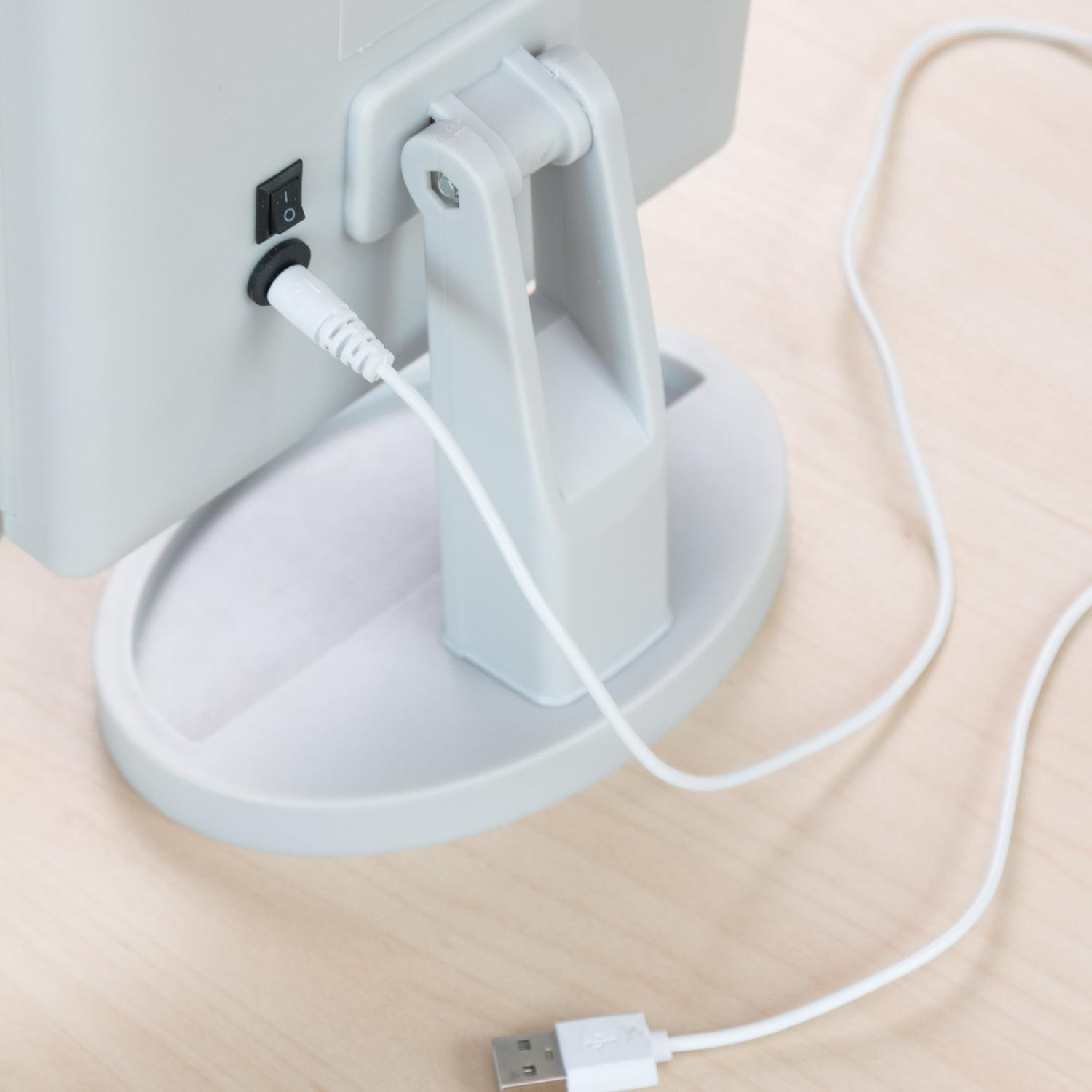 Primer plano de la parte trasera de un espejo iluminado, con un puerto de carga y un cable USB enchufado.