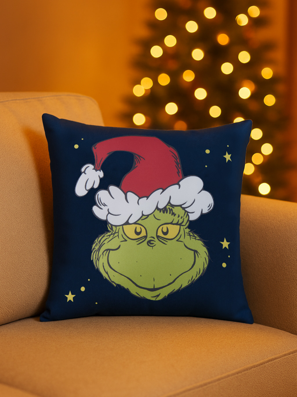 Ein Grinch-Kissen auf einer Couch. Das Grinch-Gesicht trägt einen Weihnachtsmannhut. Im Hintergrund ist ein Weihnachtsbaum mit Lichtern.