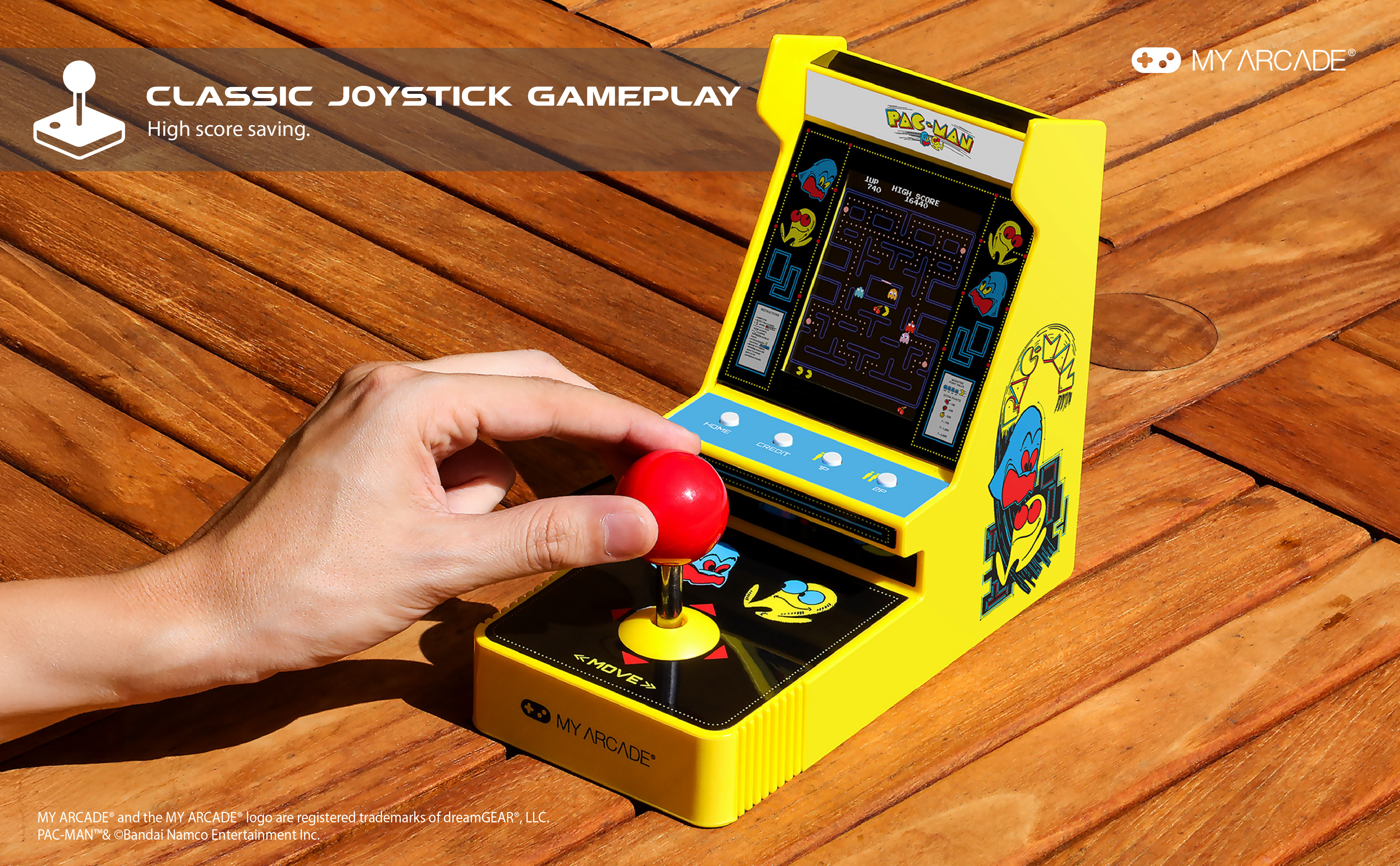Die Hand einer Person bedient einen roten Joystick an einem gelben Pac-Man-Arcade-Spiel. Das Spiel steht auf Holz.