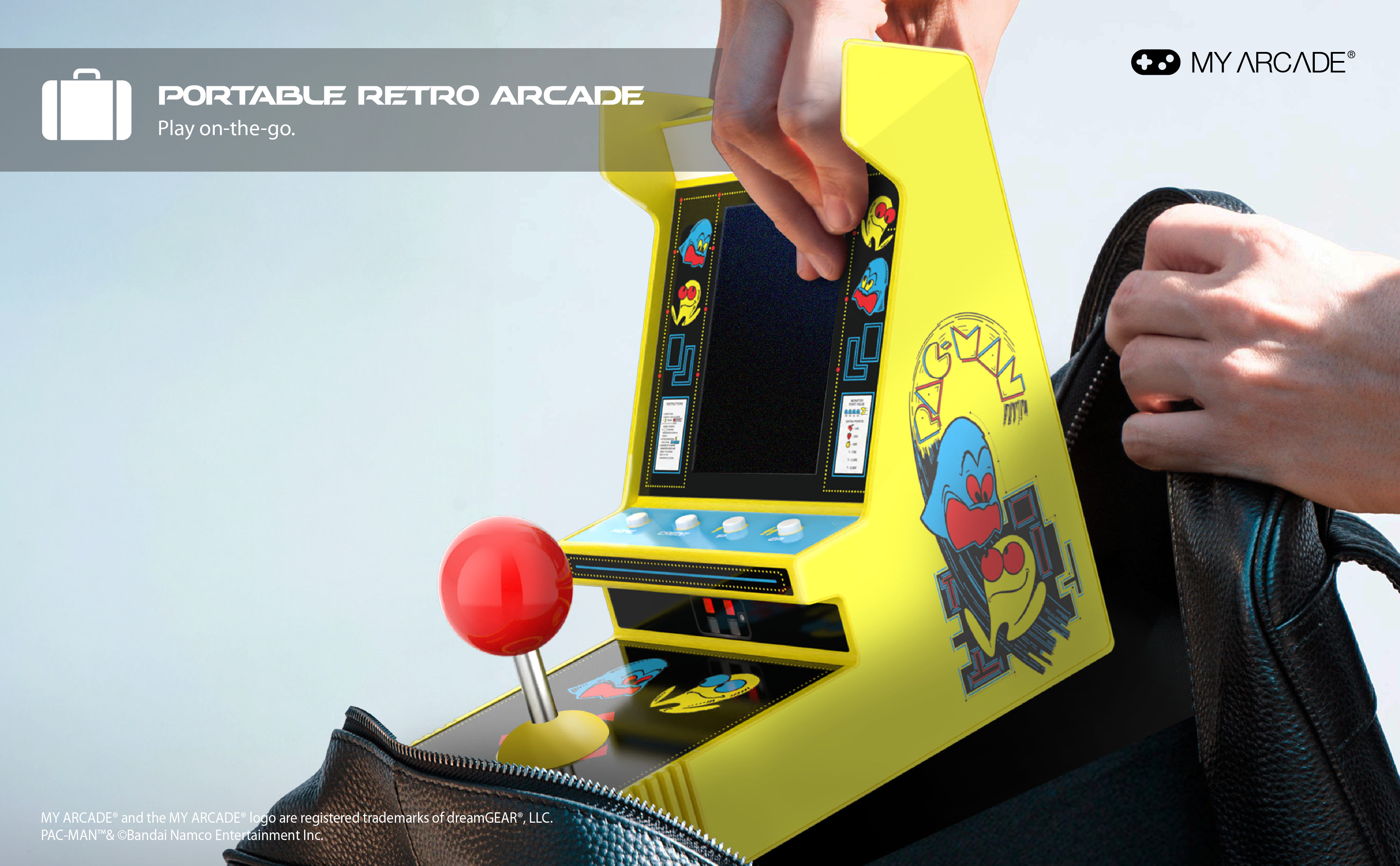 Ein gelbes Pac-Man-Arcade-Spiel wird von einer Person in eine schwarze Tasche gelegt. Das Spiel hat einen roten Joystick.
