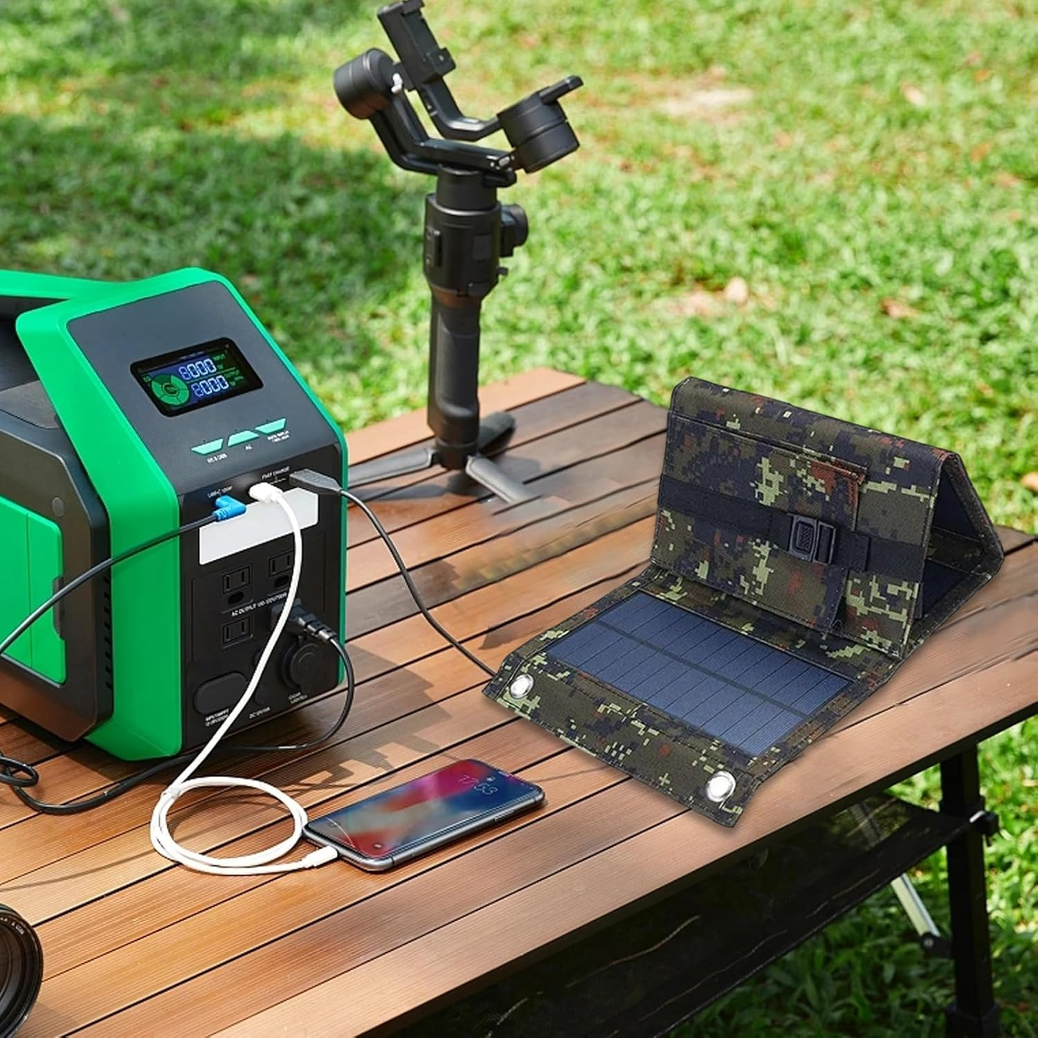Ein Solarpanel liegt auf einem Holztisch neben einer Ladestation, einem Telefon und Kameraausrüstung.