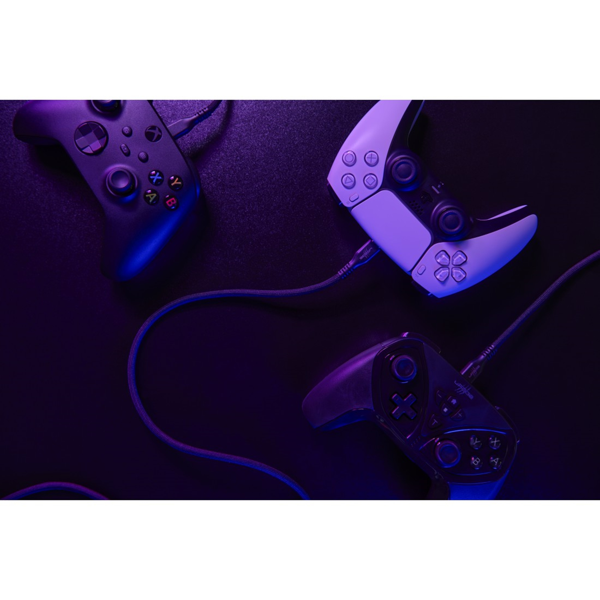 Tre controller di gioco su una superficie scura, illuminati di viola e blu. Cavi visibili.