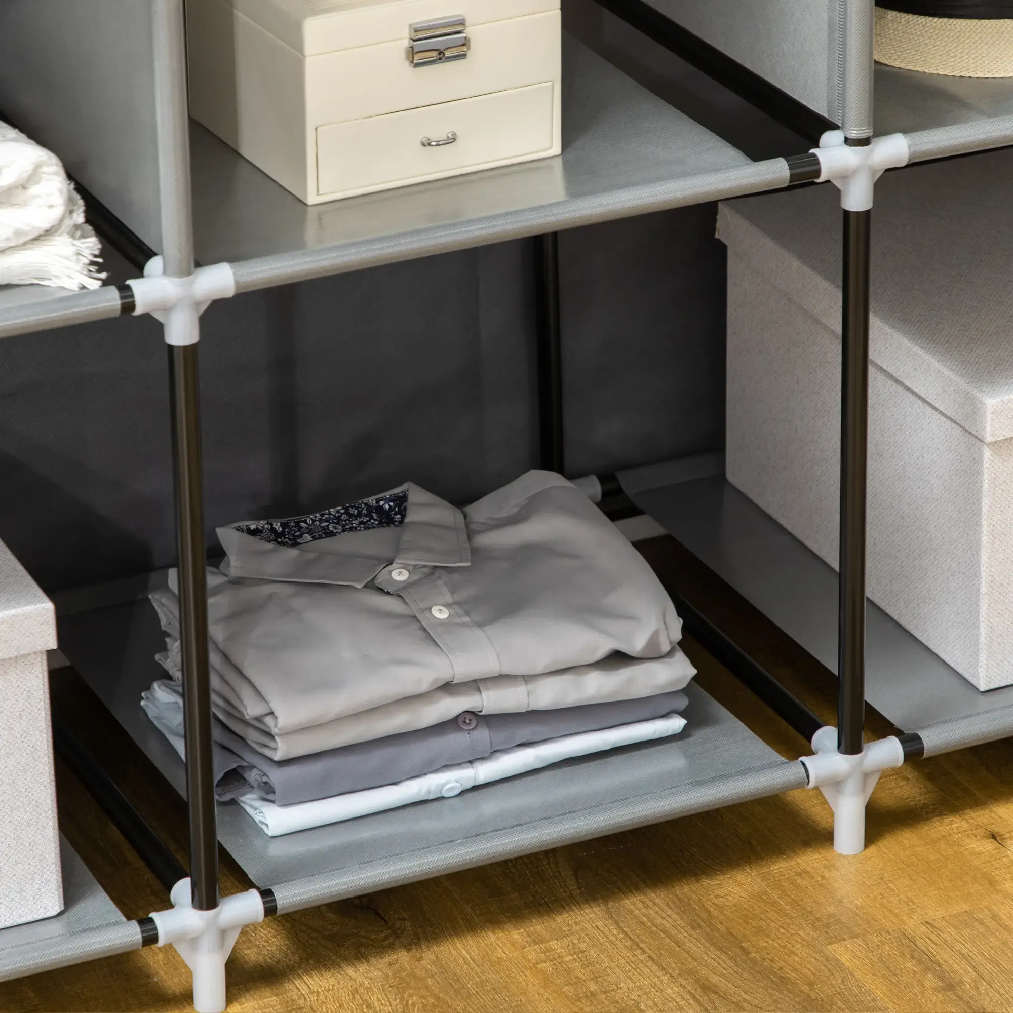 Ein Schrank mit mehreren Regalen mit Kleidung und Kisten. Gefaltete Hemden liegen auf einem Regal. Der Rahmen ist grau.
