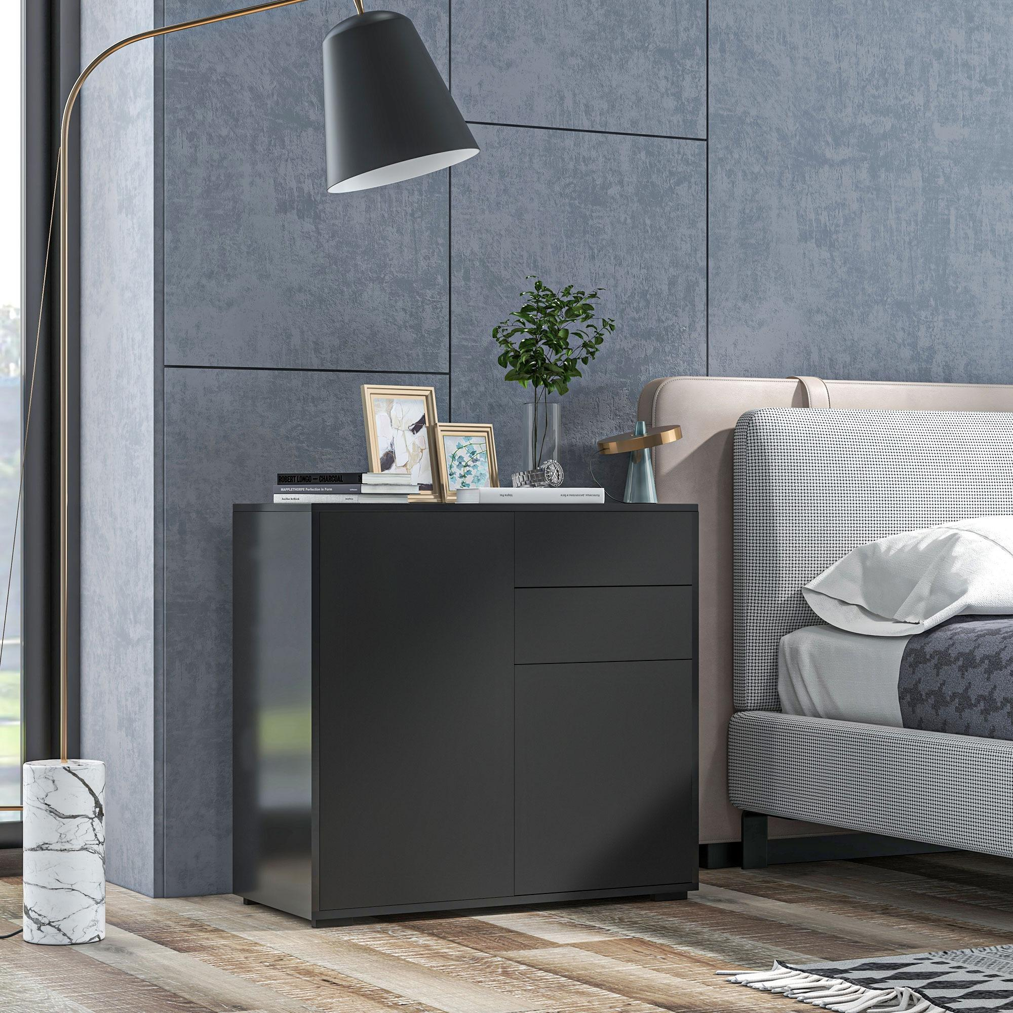 Ein schwarzer Schrank mit Tür und Schublade. Eine Lampe und Dekorationsartikel stehen daneben vor grauem Hintergrund.