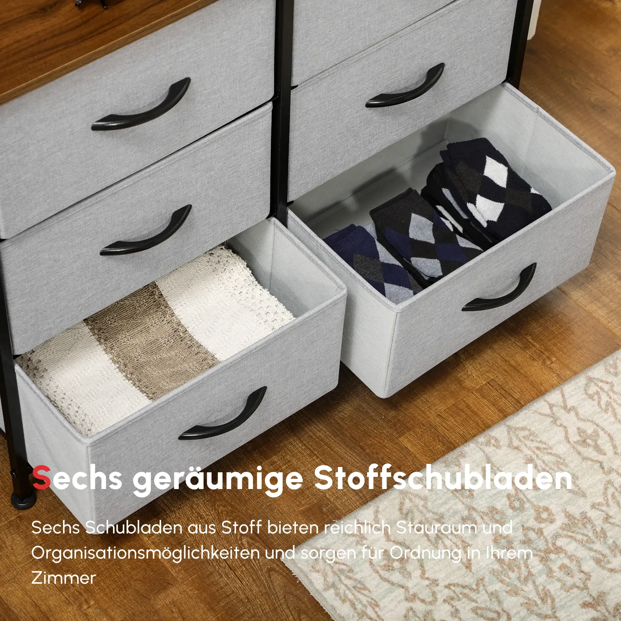 Graue Kommode mit sechs Schubladen. Zwei Schubladen sind geöffnet und zeigen Decken und Socken.