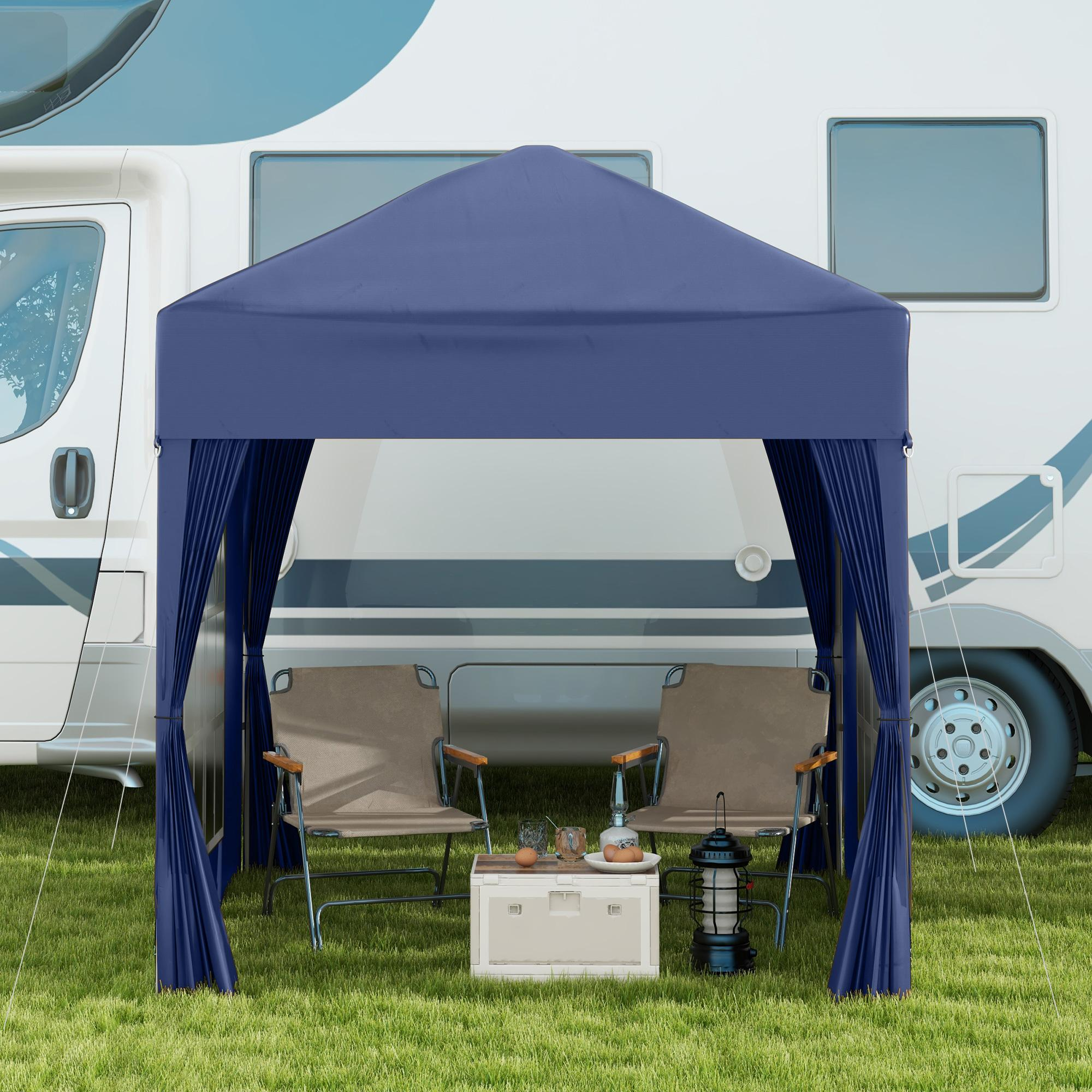 Ein blaues Zelt mit zwei Stühlen, einem Tisch und einem Wohnwagen im Hintergrund.