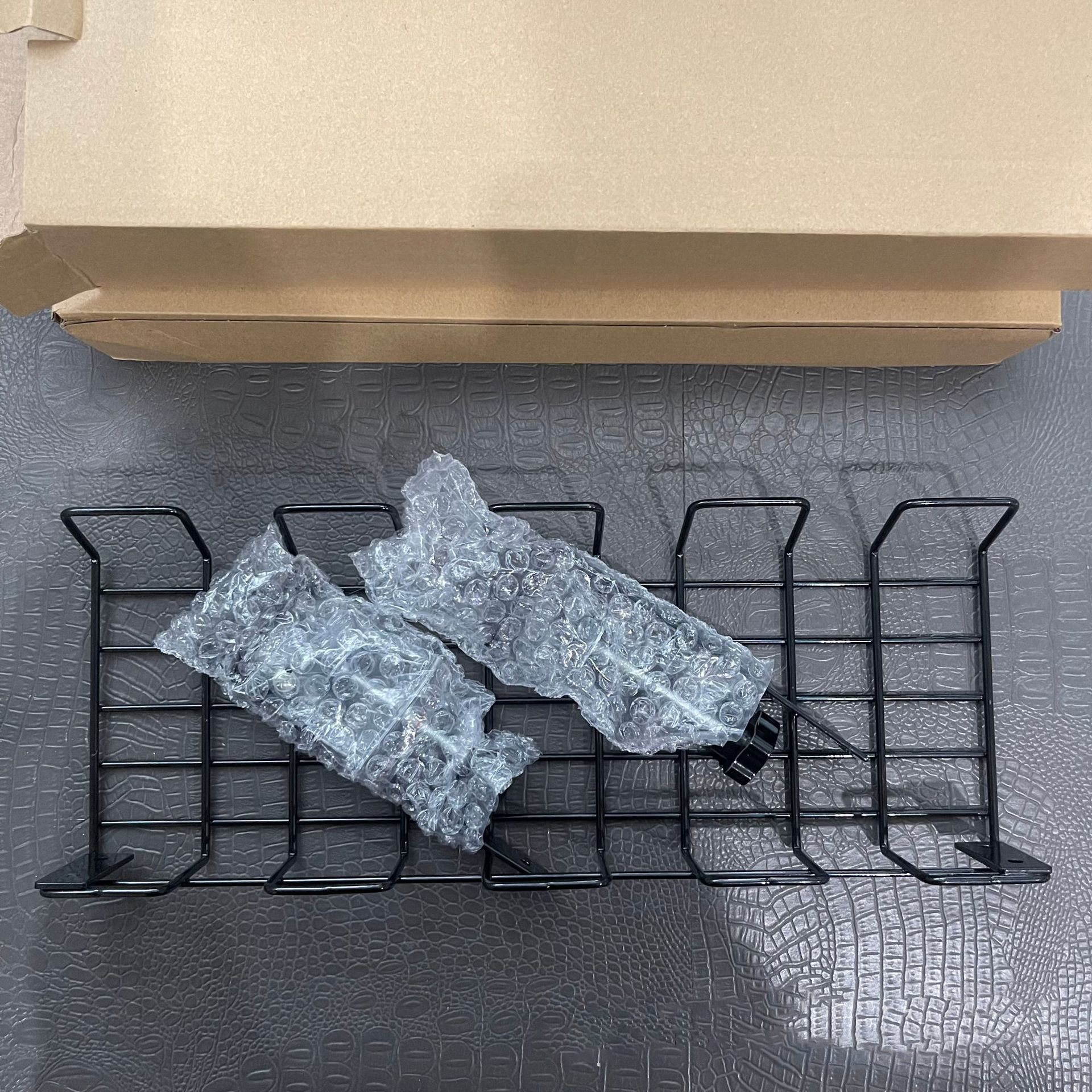 Zwei schwarze Drahtkabelwannen, verpackt mit Luftpolsterfolie, liegen auf einer grauen Oberfläche.