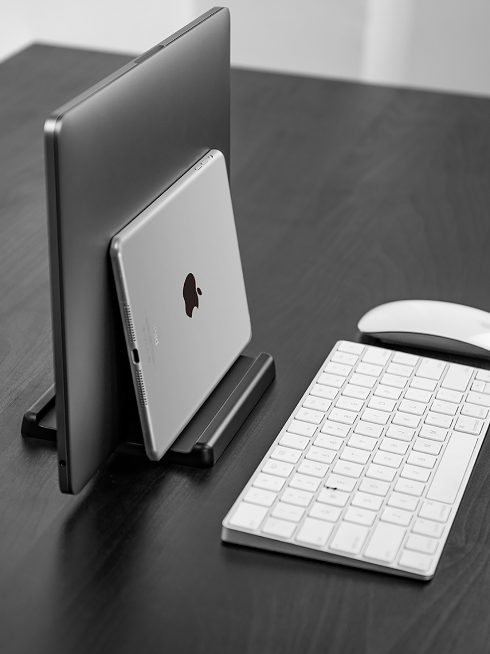 Laptop und Tablet auf einem schwarzen Ständer, mit Tastatur und Maus auf einem Schreibtisch.