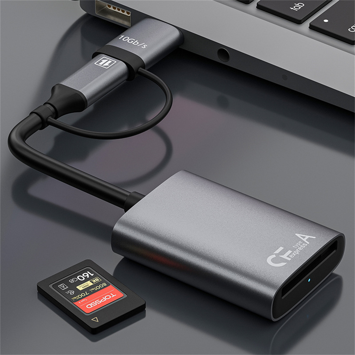 Ein grauer Kartenleser ist mit einem Laptop verbunden, mit einer roten SD-Karte in der Nähe auf einer dunklen Oberfläche.