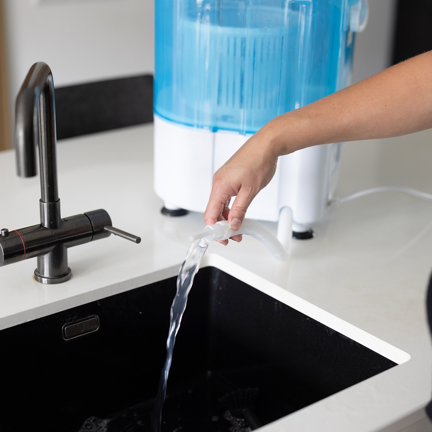 A person is pouring water into a black sink from a small washing machine.