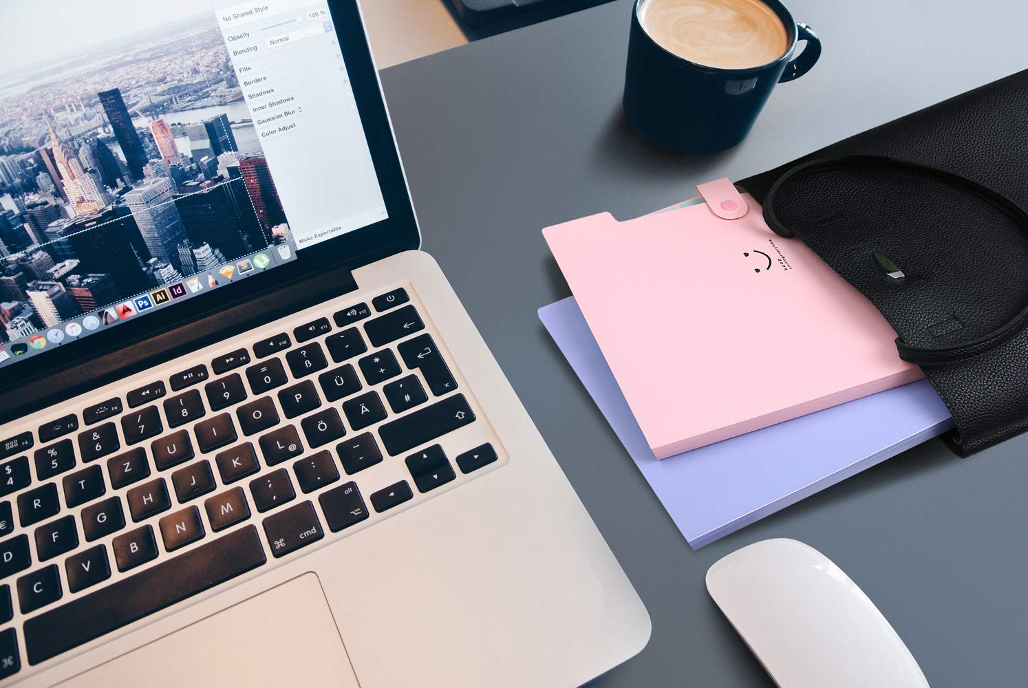 Laptop, rosa Ordner, Stift, Tasse auf grauem Schreibtisch.