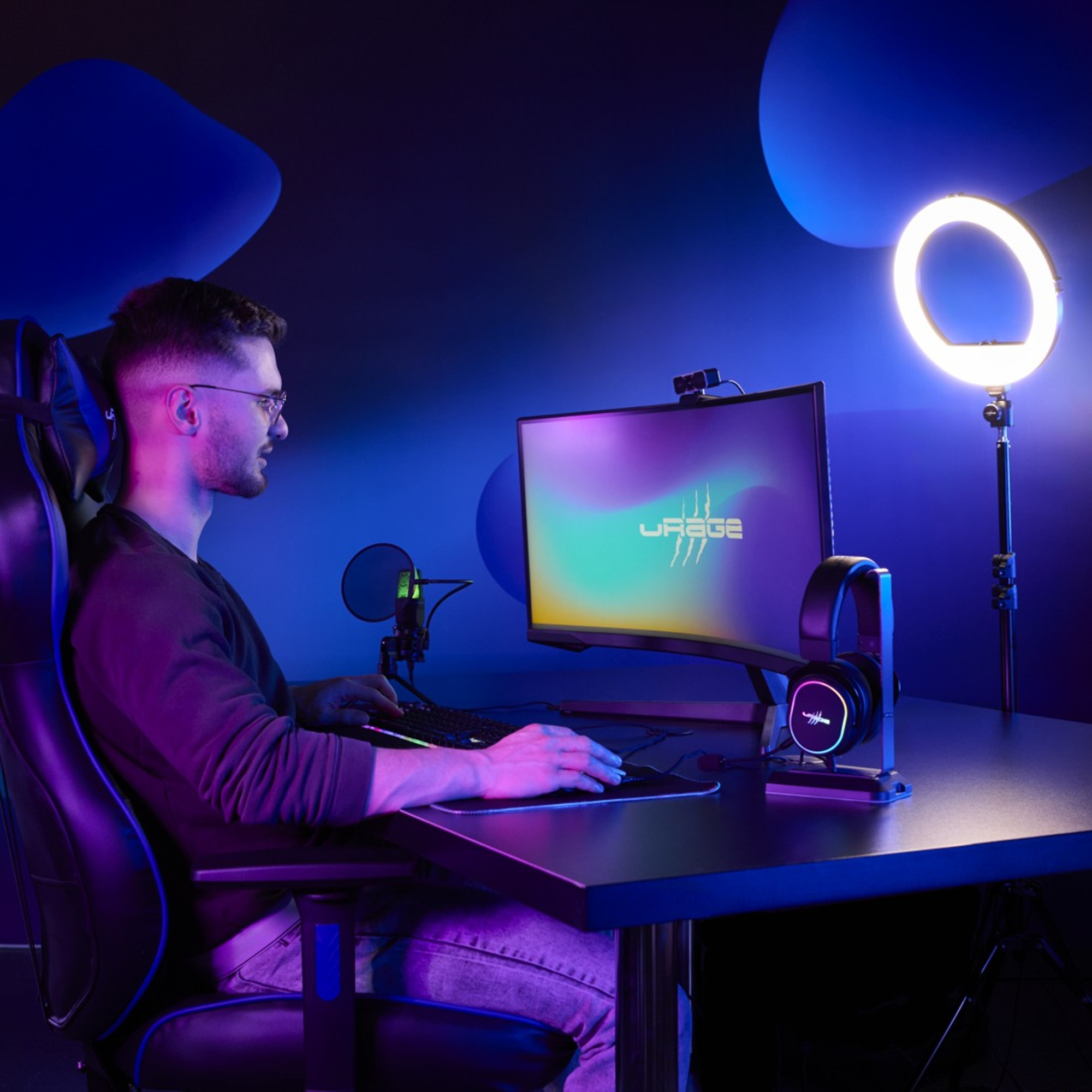 Ein Mann mit Brille benutzt einen Computer mit Monitor, Mikrofon, Headset und Ringlicht.