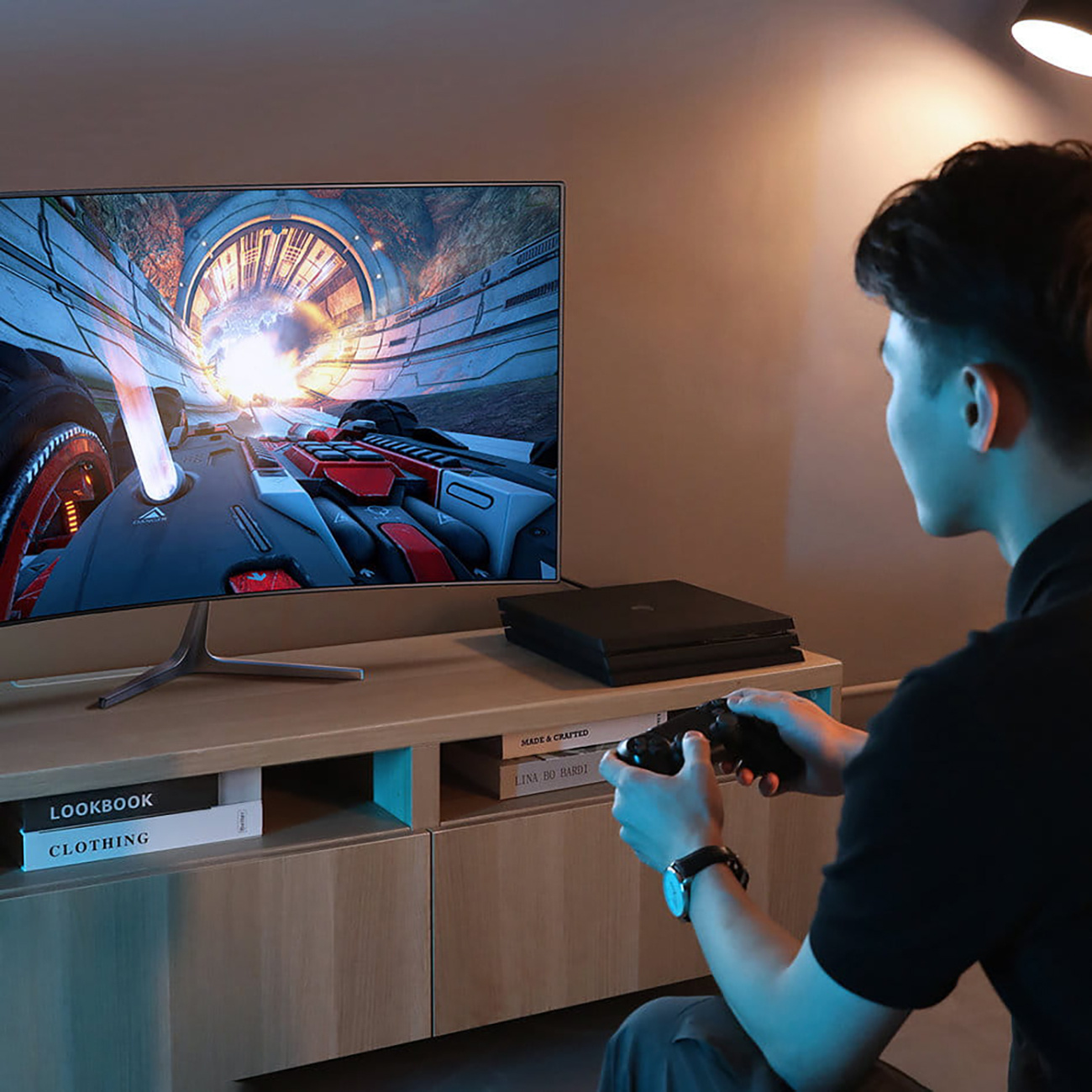 Mężczyzna gra w grę na telewizorze z konsolą i kontrolerem. Widoczna czarna konsola i kontroler.