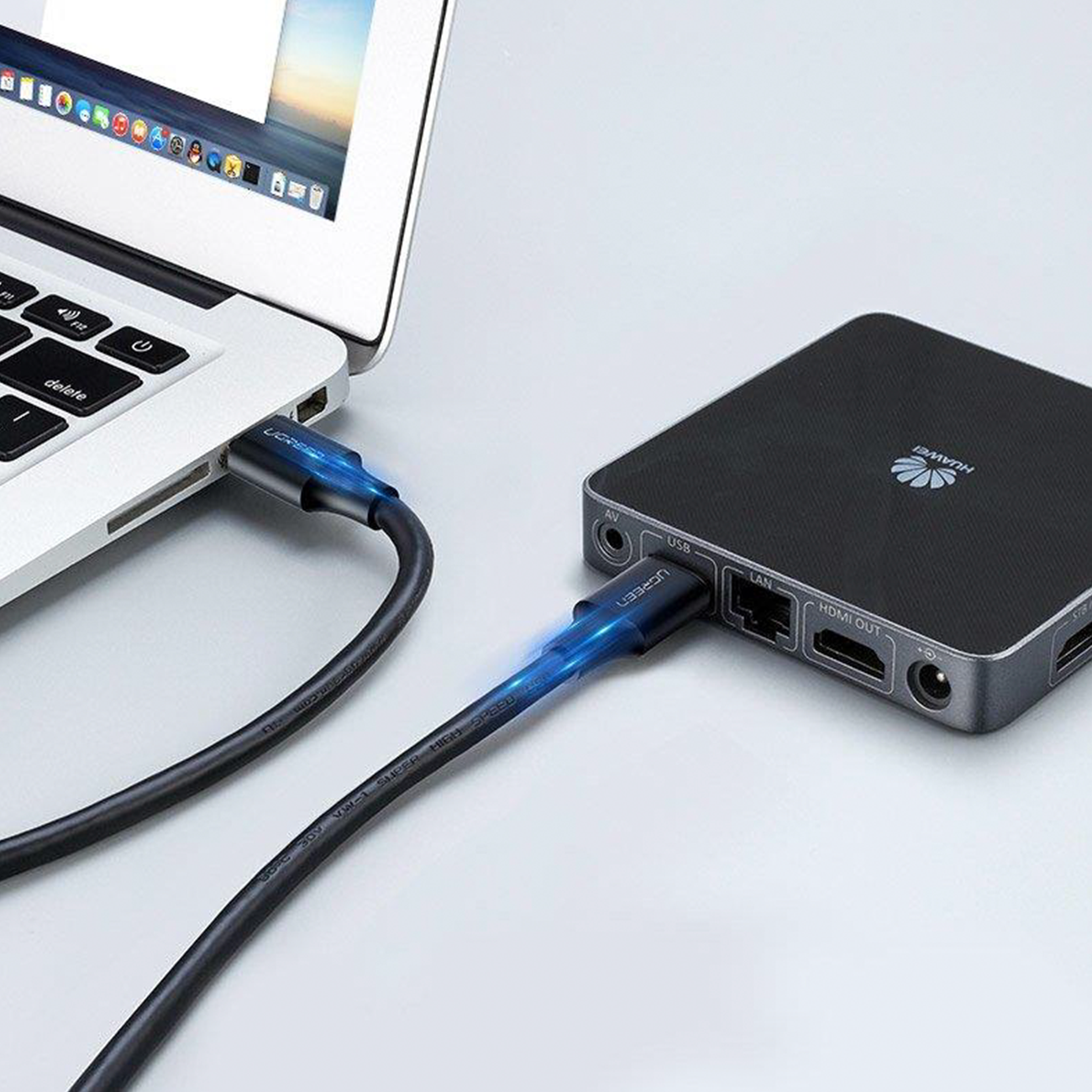 Czarny kabel USB-C podłączony do laptopa i czarnego urządzenia. Kabel ma niebieskie światło.