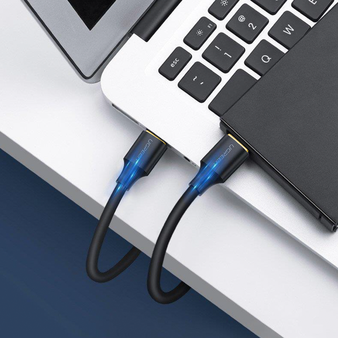 Czarny kabel USB-C podłączony do laptopa i czarnego urządzenia, z niebieskim światłem.