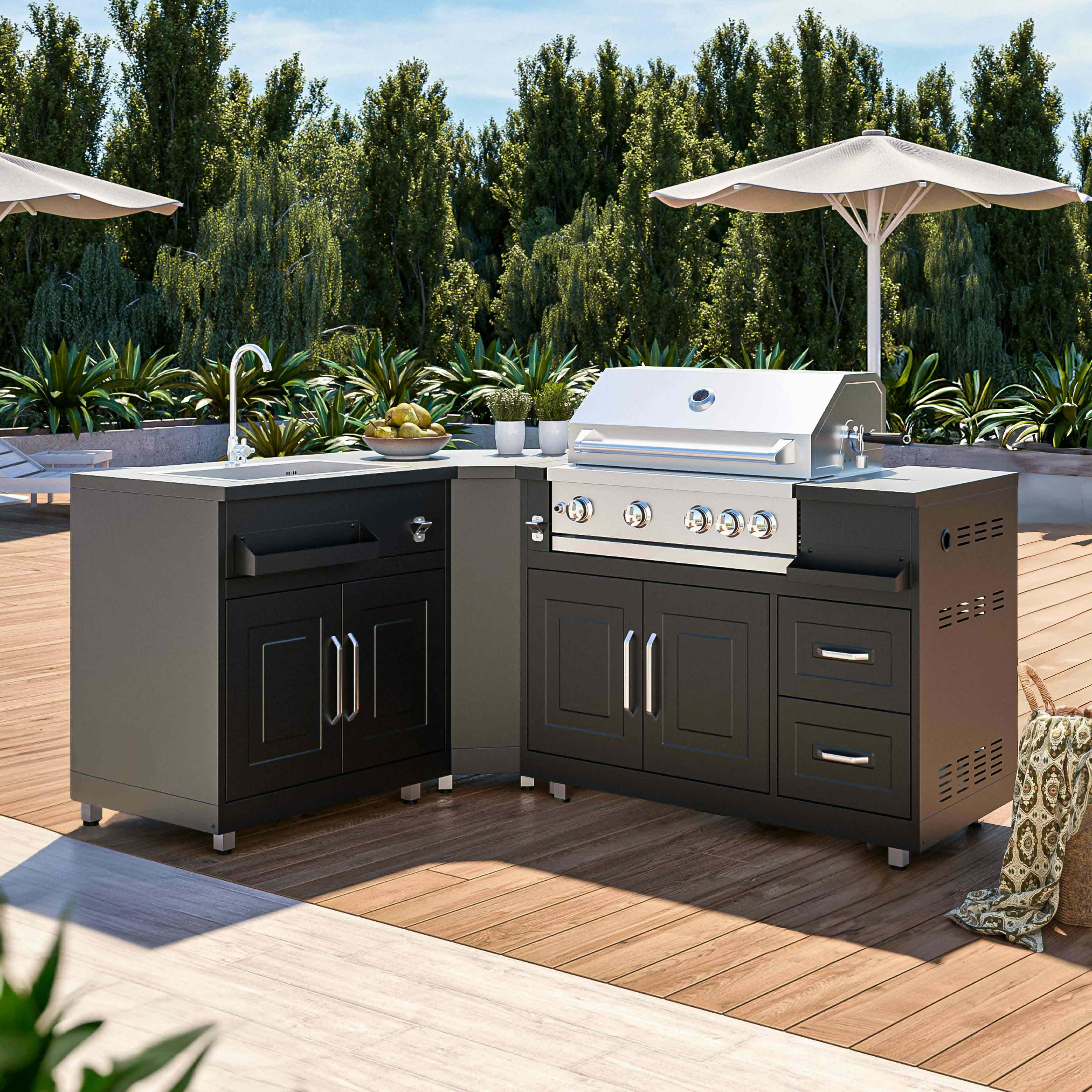 Outdoor-Küchenaufbau mit Grill, Spüle und Schränken auf Holzterrasse. Bäume im Hintergrund.
