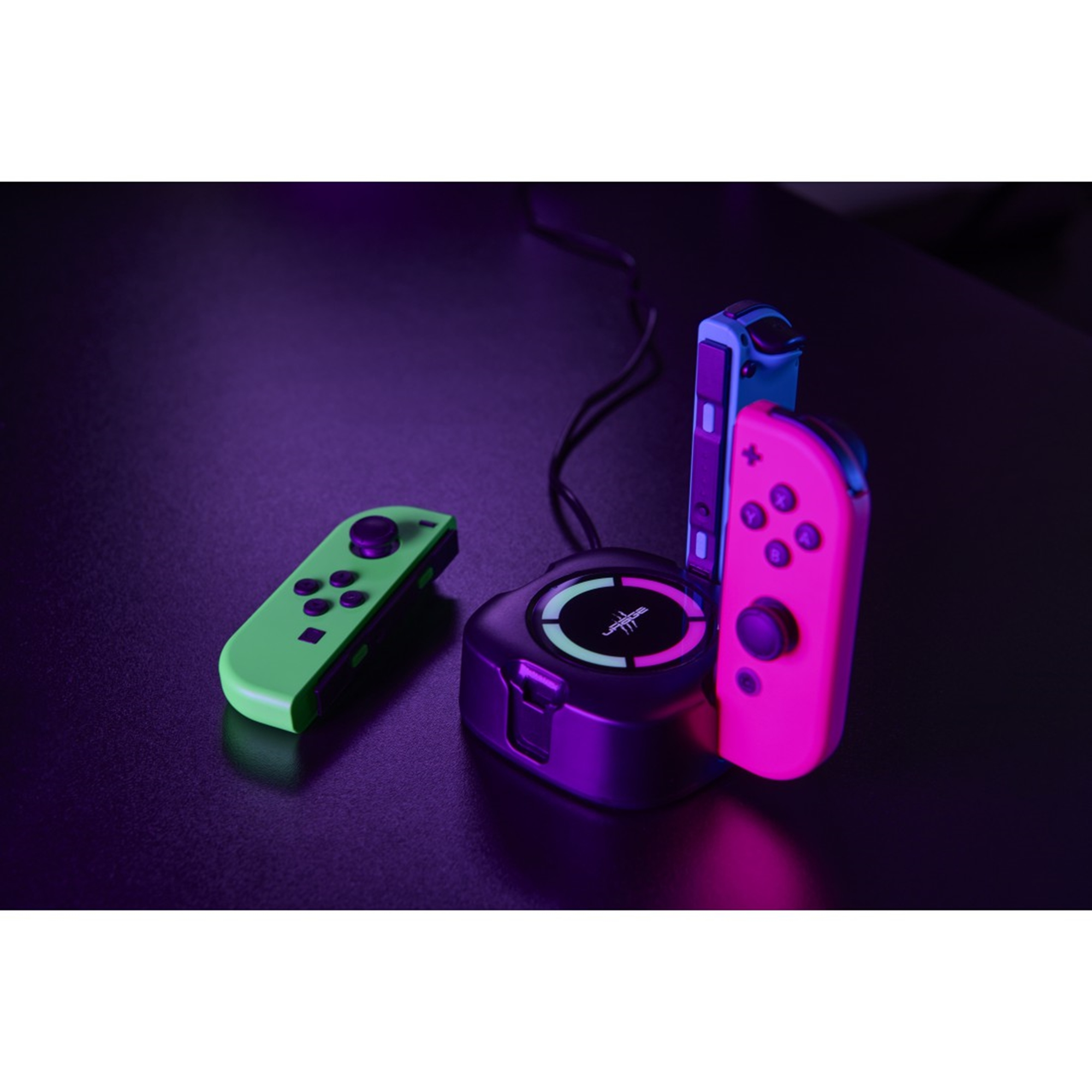 Eine Ladestation mit drei Gamecontrollern. Controller sind grün, rosa und blau. Dunkler Hintergrund.