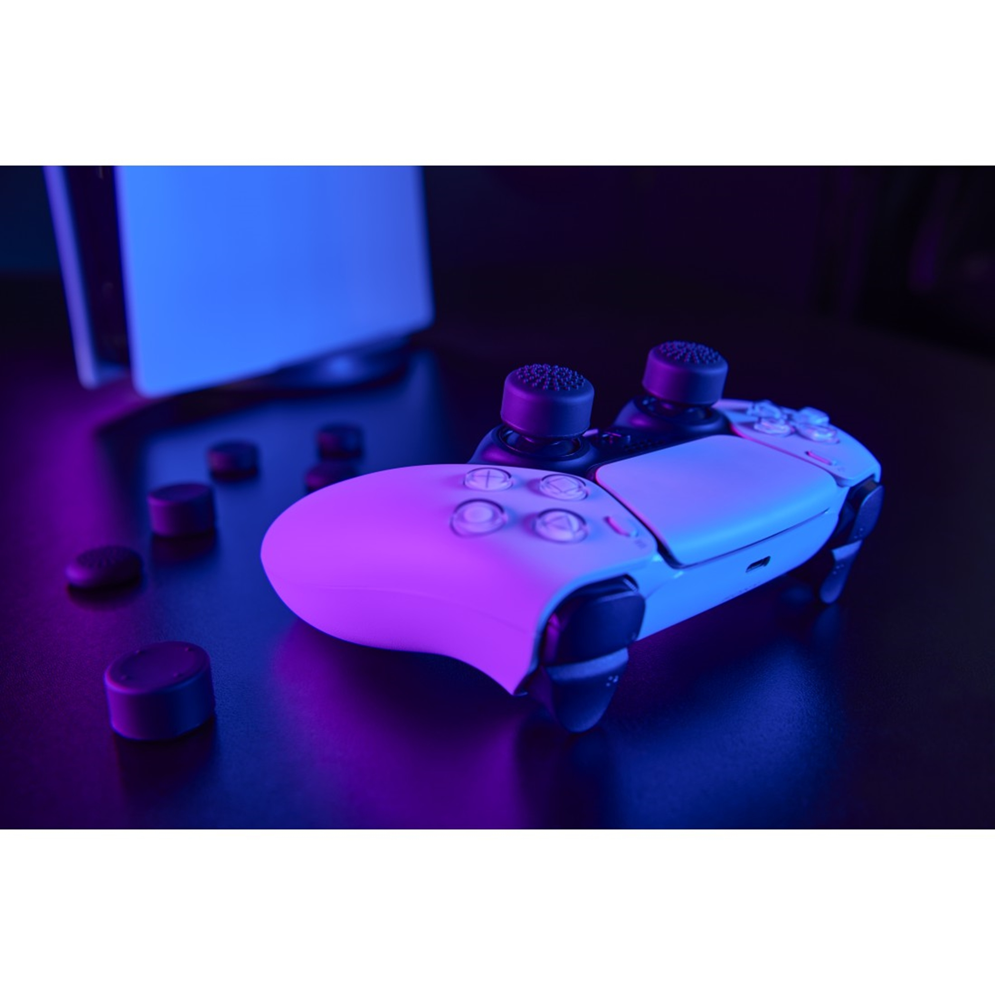 Ein weißer Gamecontroller mit schwarzen Daumensticks und ein paar zusätzlichen Daumensticks auf dunkler Oberfläche, im Hintergrund eine weiße Konsole.