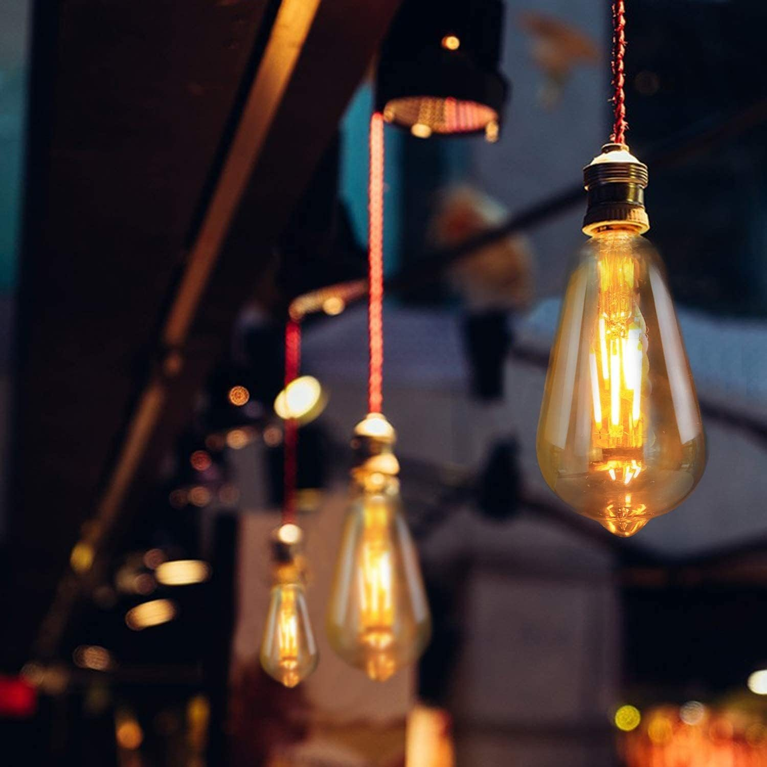 Drei Edison-Glühbirnen hängen von der Decke. Sie sind beleuchtet und strahlen ein warmes, orangefarbenes Licht aus. Der Hintergrund ist unscharf.