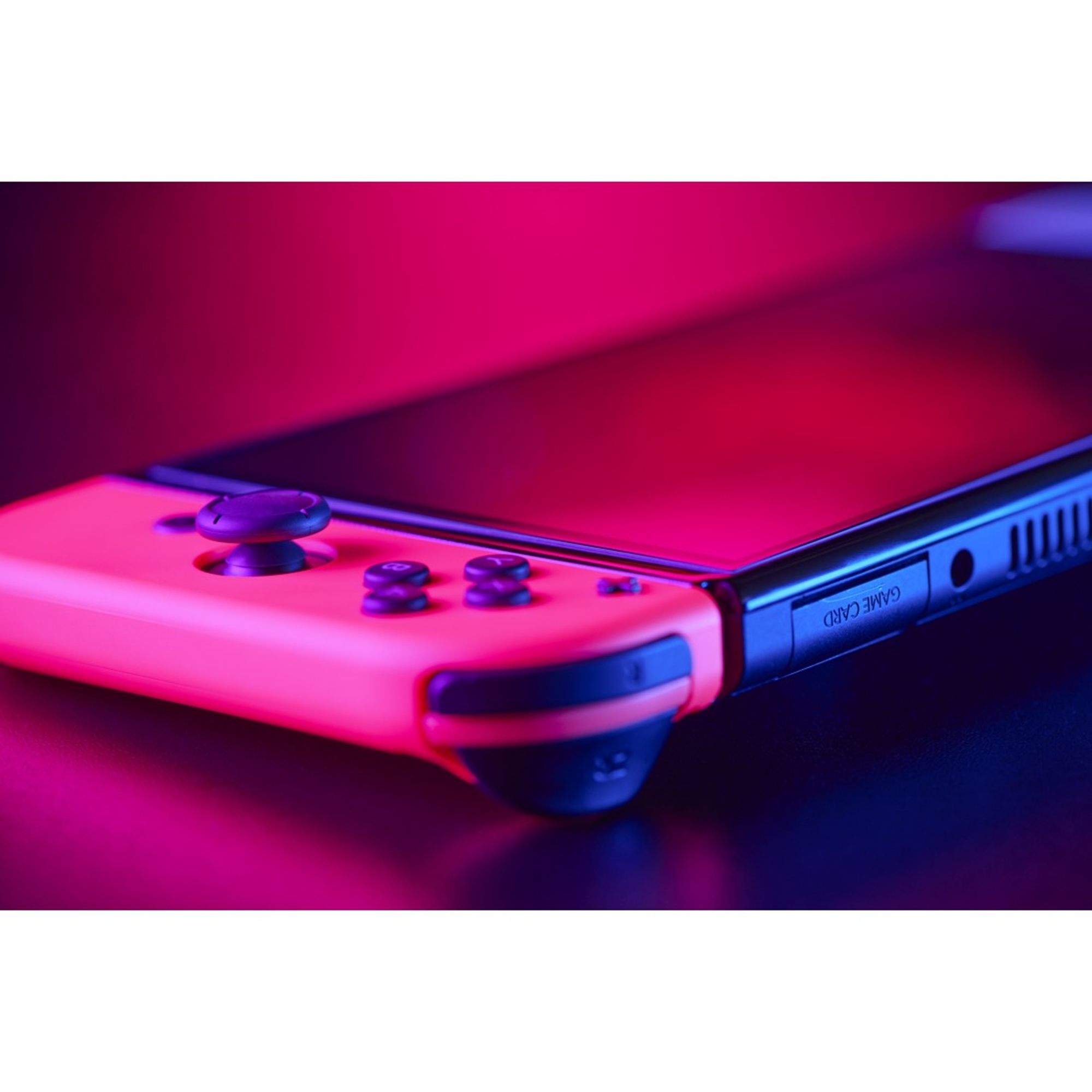 Nahaufnahme eines rosa Nintendo Switch Controllers mit schwarzen Knöpfen auf dunkler Oberfläche mit rosa und blauer Beleuchtung.
