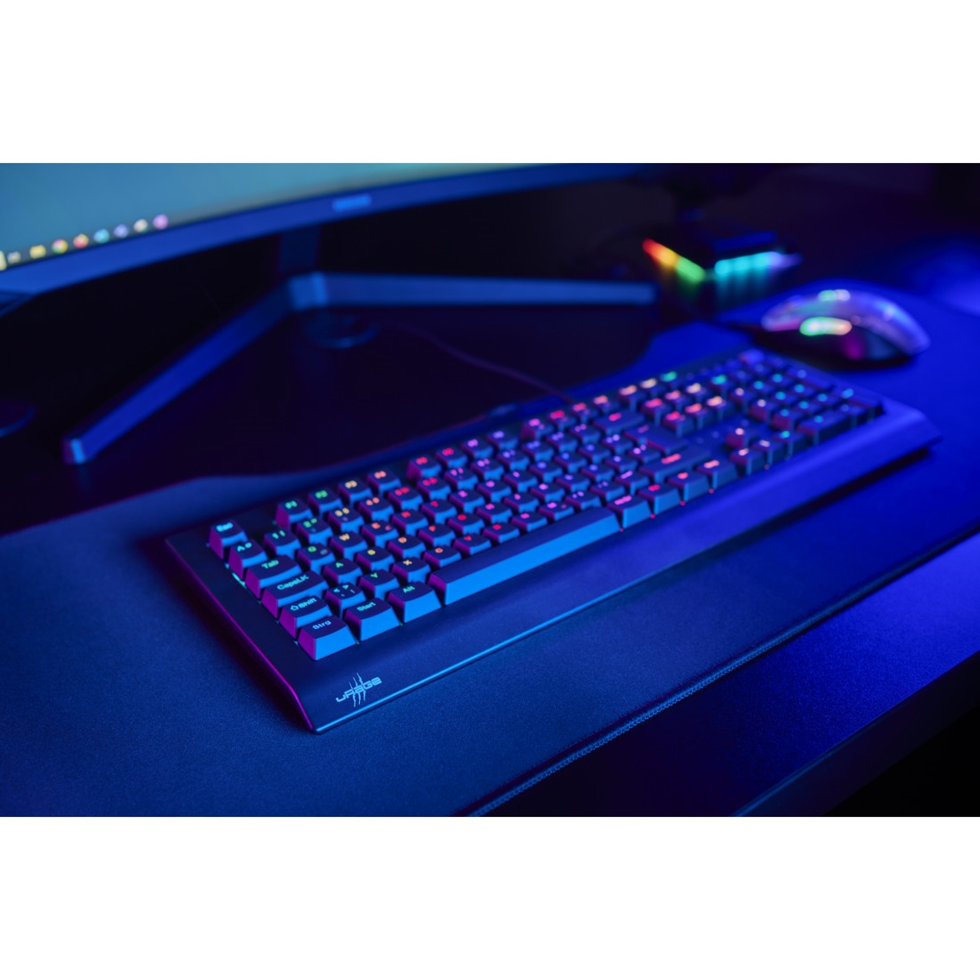 Schwarze Tastatur mit beleuchteten Tasten auf einem schwarzen Schreibtisch. Ein Monitor und eine Maus sind im Hintergrund.