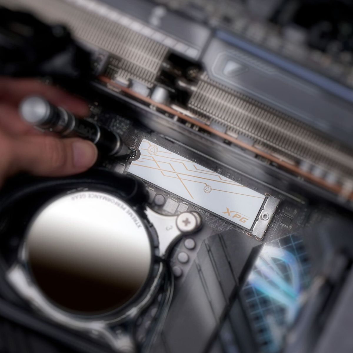Dysk SSD XPG montowany w komputerze. Jest biały ze złotymi liniami. Pokazana jest dłoń.