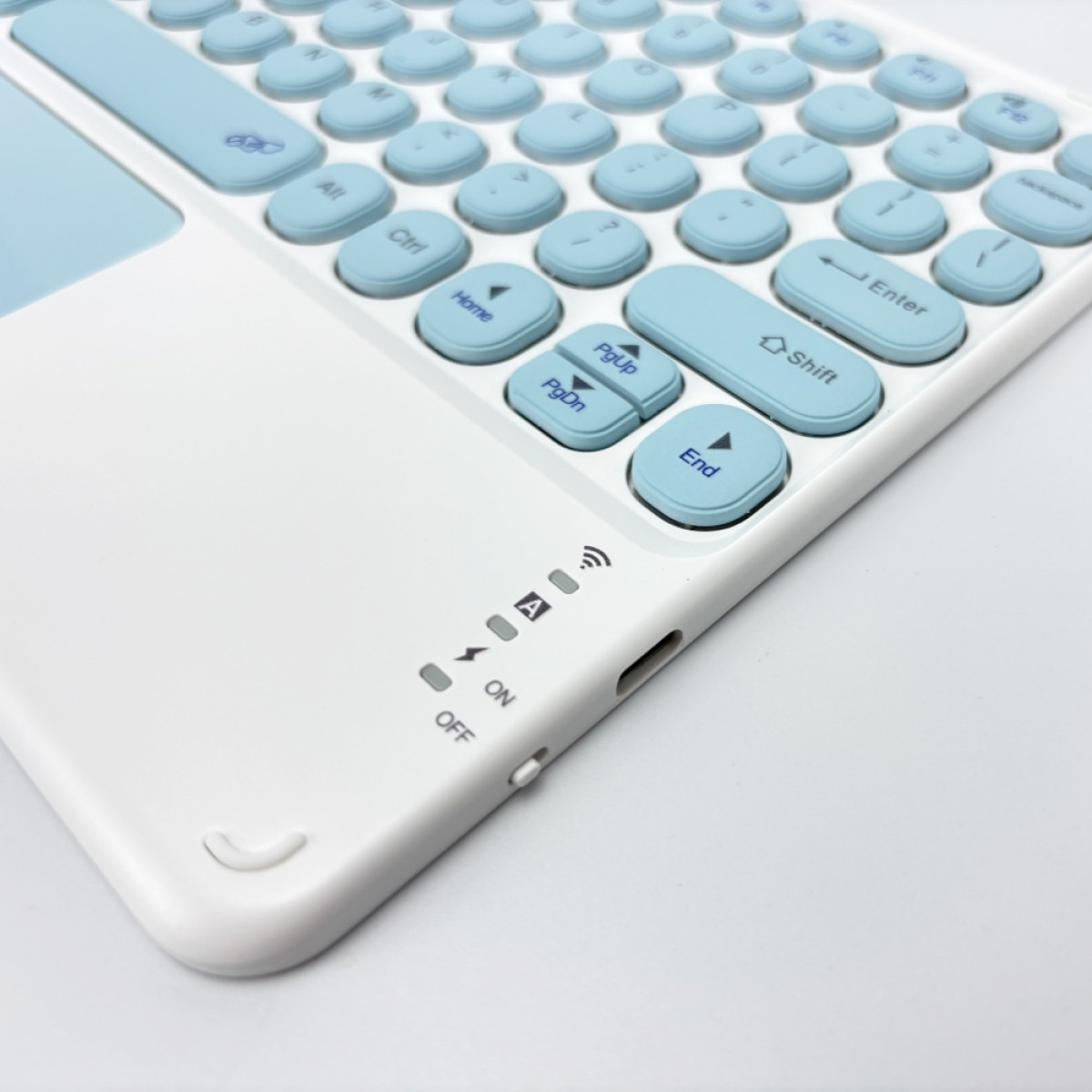Wit toetsenbord met lichtblauwe toetsen, een touchpad en stroom/verbindingsindicatoren. Op een wit oppervlak.