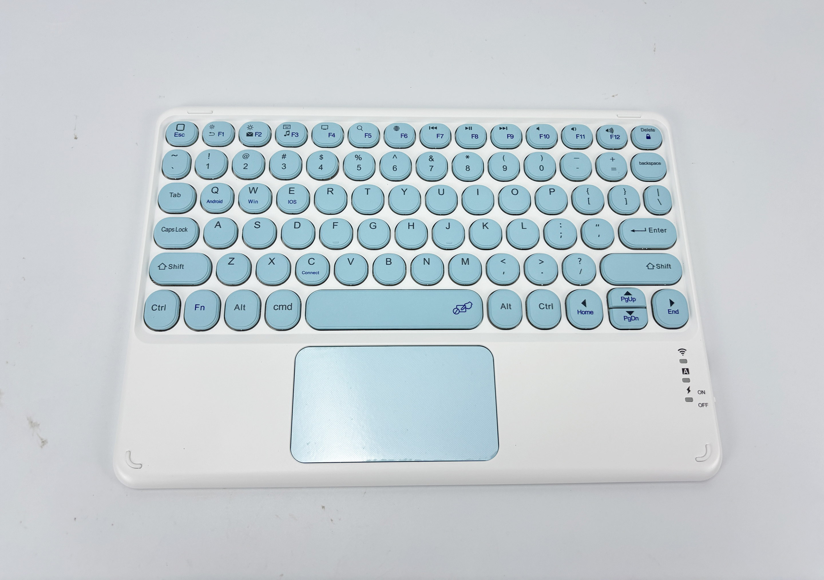 Een wit toetsenbord met lichtblauwe toetsen en een trackpad. Het toetsenbord ligt op een wit oppervlak.